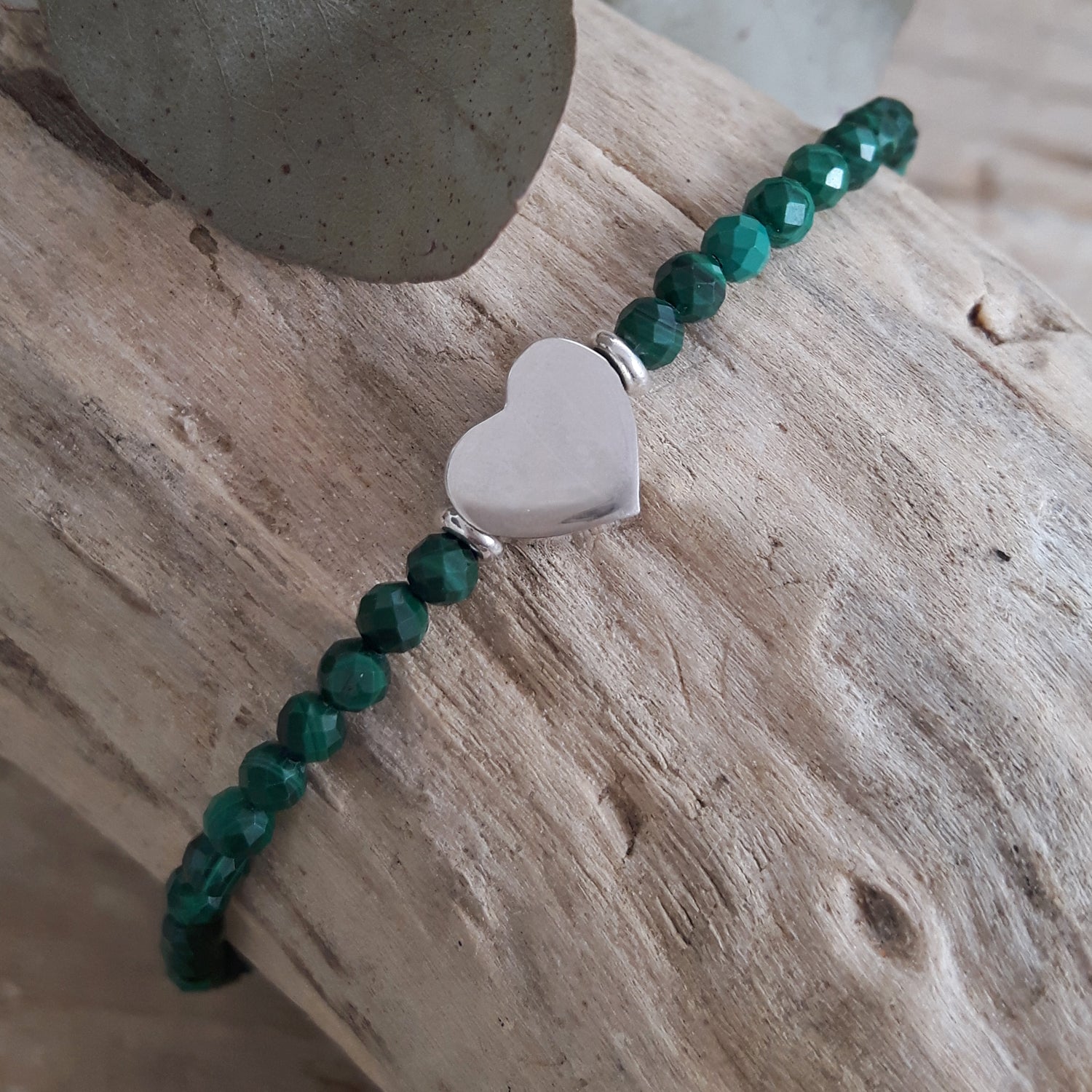 Malachite beaded bracelet with a sterling silver heart charm on a wooden surface