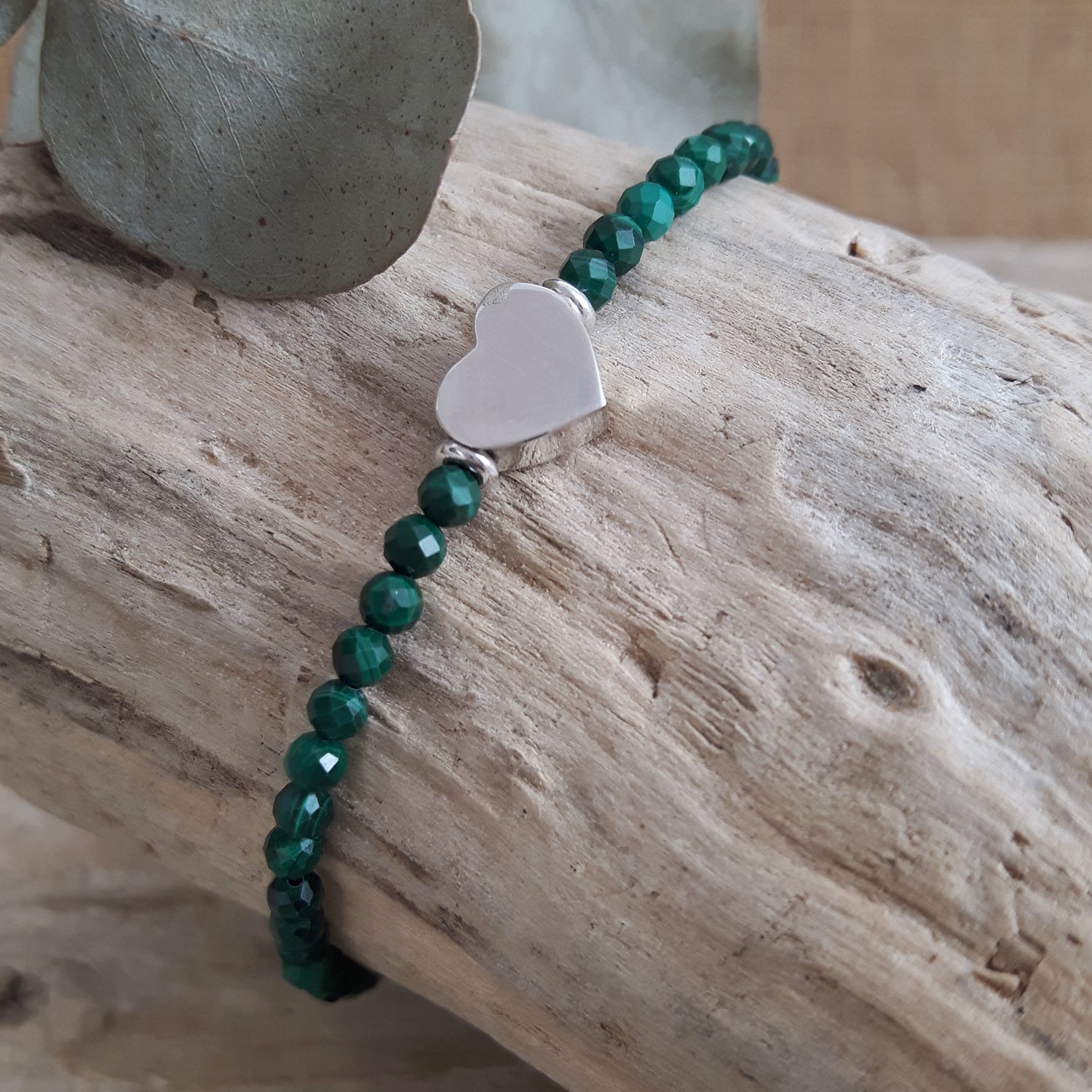 Malachite beaded bracelet with a sterling silver heart charm on a wooden surface