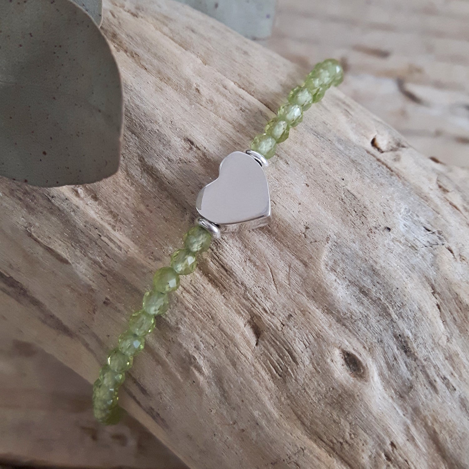 Green peridot birthstone beaded bracelet with a sterling silver heart charm on a wooden surface