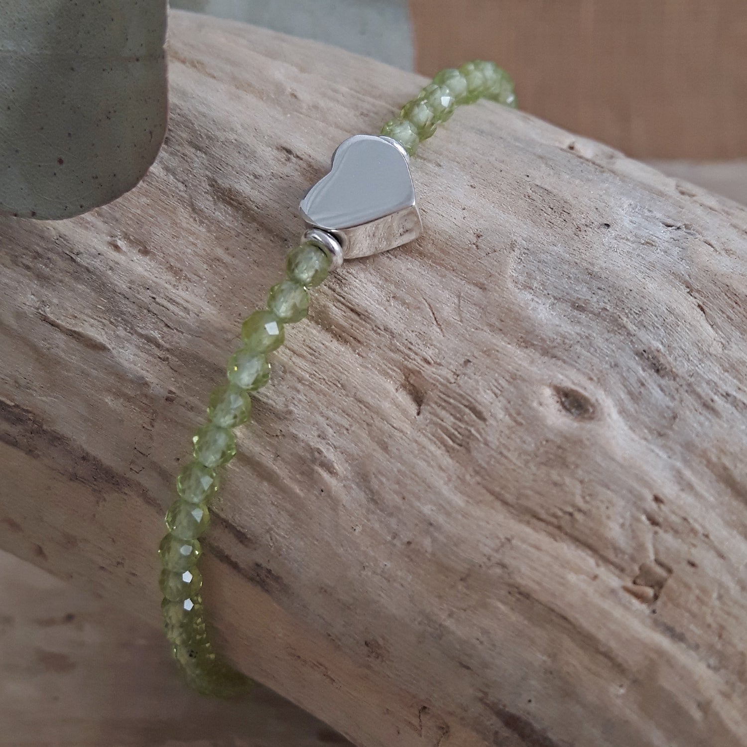 Green Peridot beaded bracelet with a sterling silver heart charm on a wooden surface
