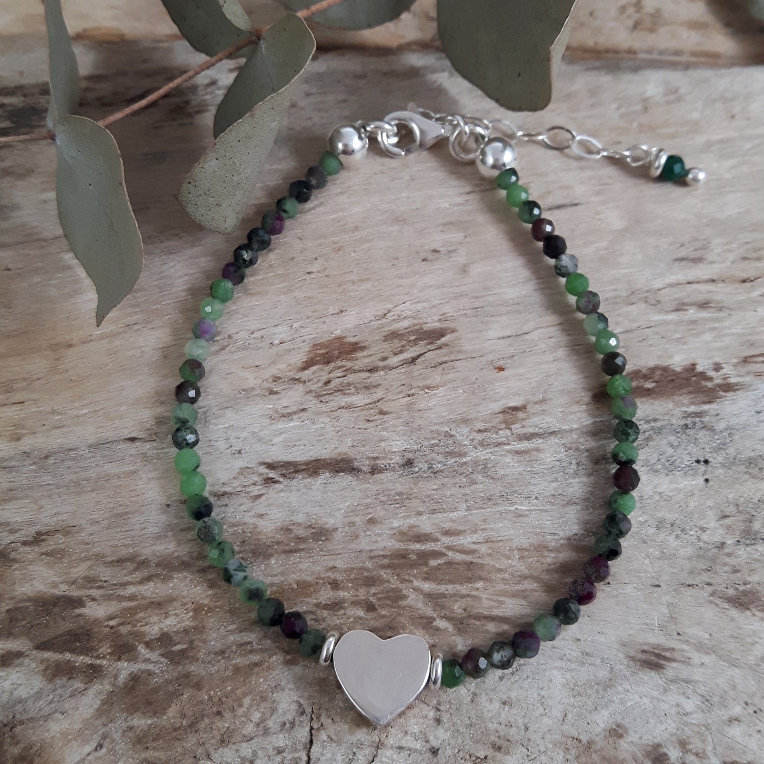Ruby Zoisite July Birthstone Bracelet with sterling silver heart charm on a wooden surface