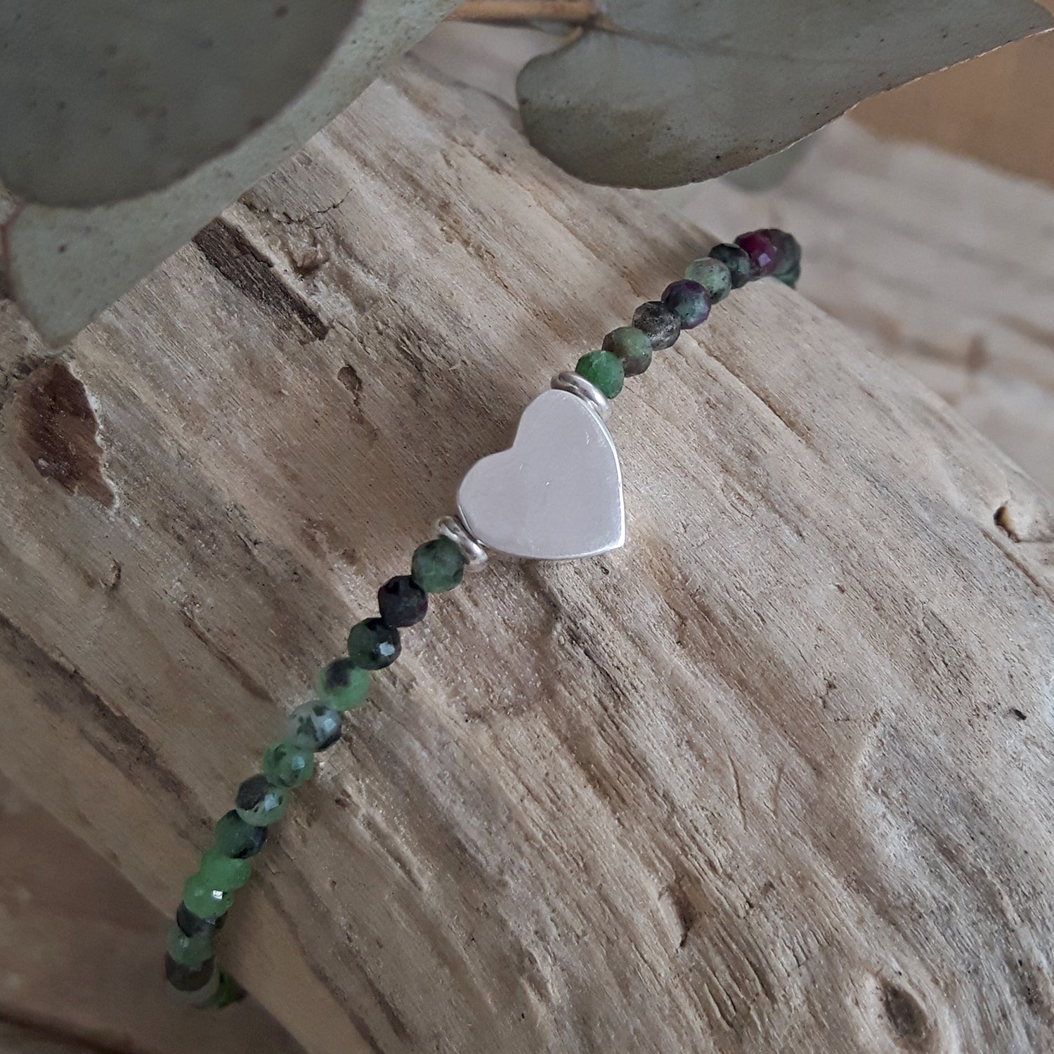 Ruby Zoisite birthstone bracelet with sterling silver heart charm and green gemstone beads on a wooden surface