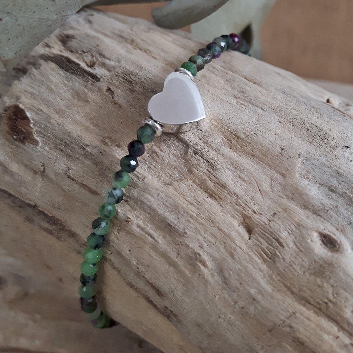 Ruby Zoisite Gemstone Beaded bracelet with a sterling heart charm on a wooden surface
