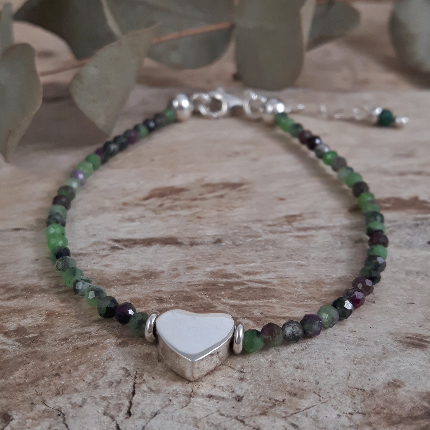 Beaded Ruby Zoisite July birthstone bracelet with a sterling silver heart charm on a wooden surface