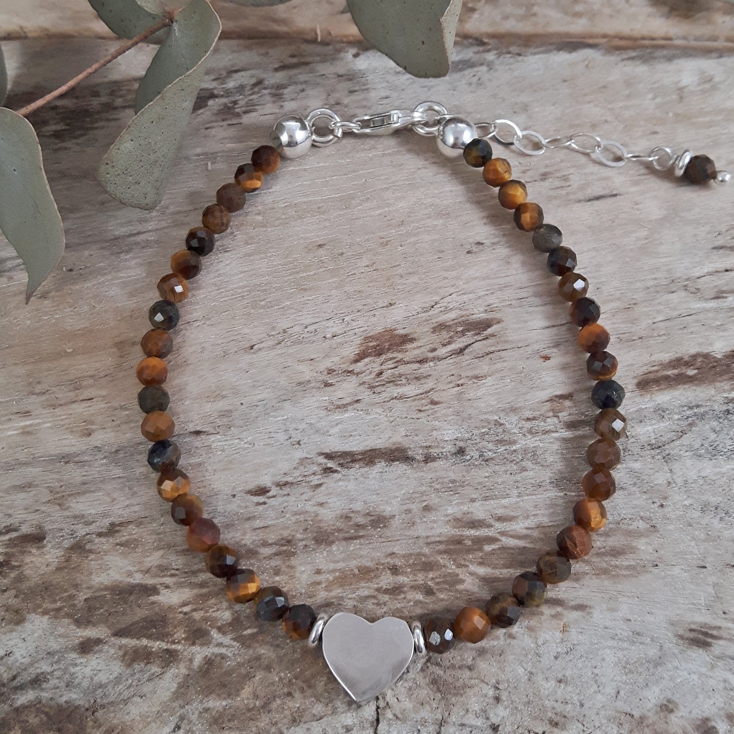 Birthstone bracelet with brown tiger's eye beads and a sterling silver heart charm on a wooden surface