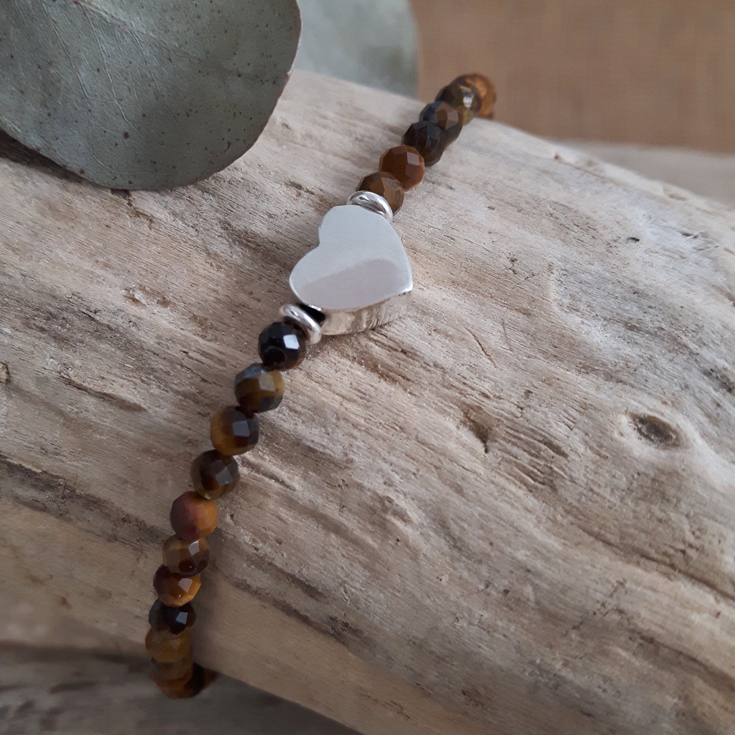 Birthstone bracelet with brown tiger's eye gemstone beads and a sterling silver heart-shaped charm on a wooden surface