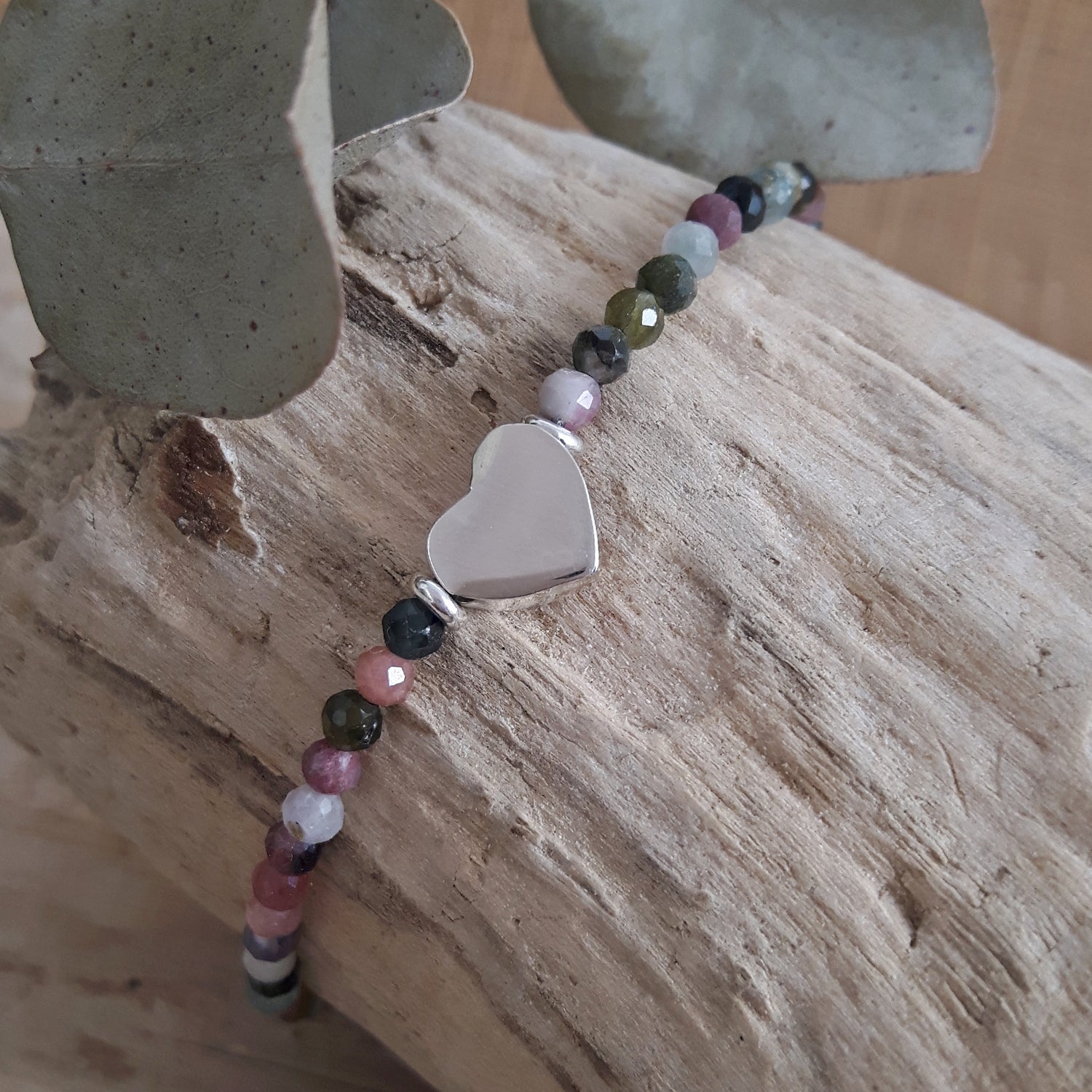 Beaded tourmaline birthstone bracelet with a sterling silver heart-shaped charm on a wooden surface