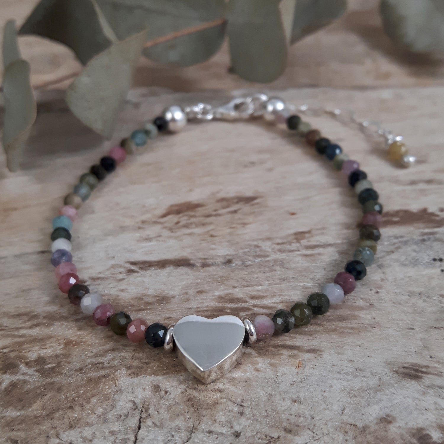 Beaded tourmaline October birthstone bracelet with a sterling silver heart-shaped charm on a wooden surface
