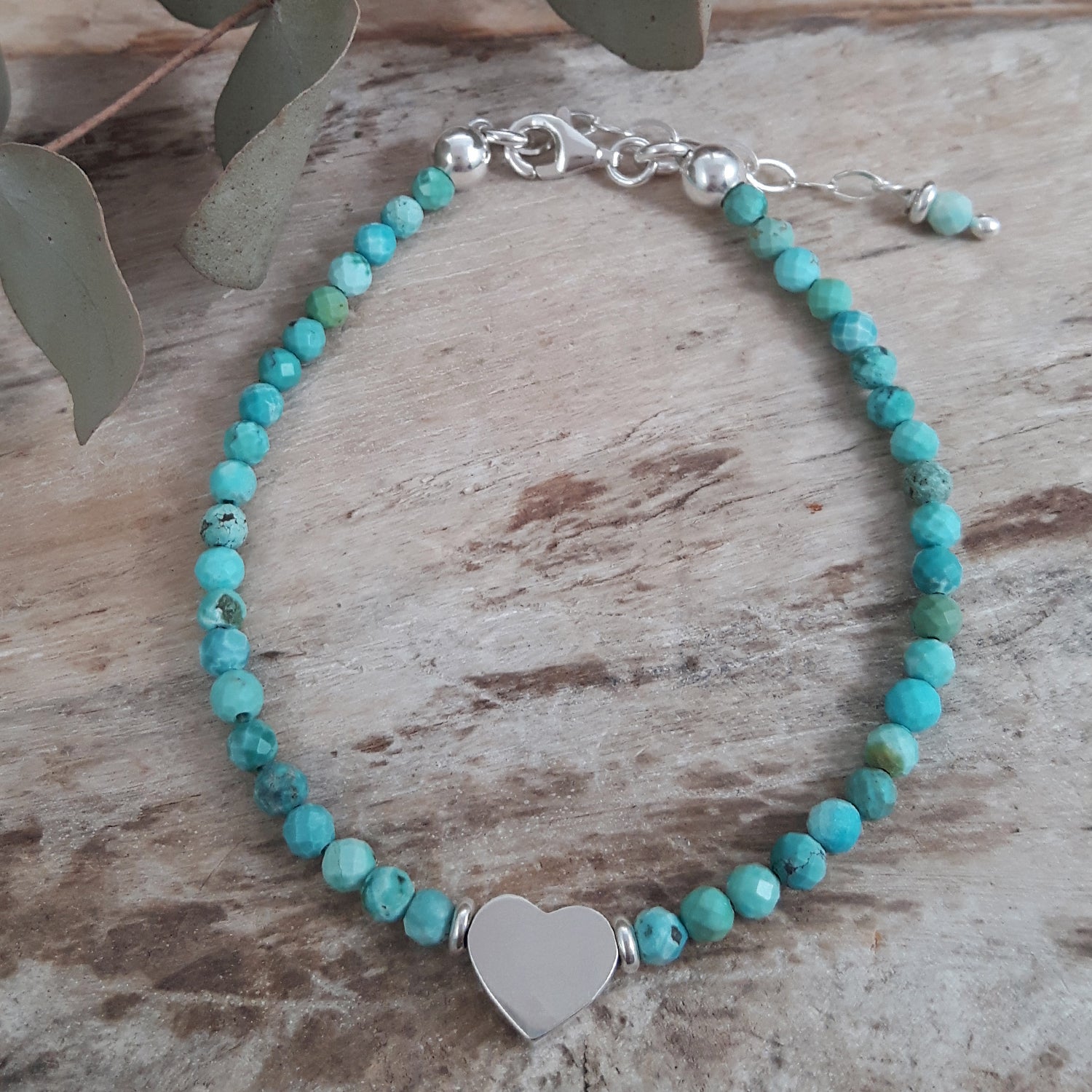 Turquoise beaded birthstone bracelet with a sterling silver heart charm on a wooden surface