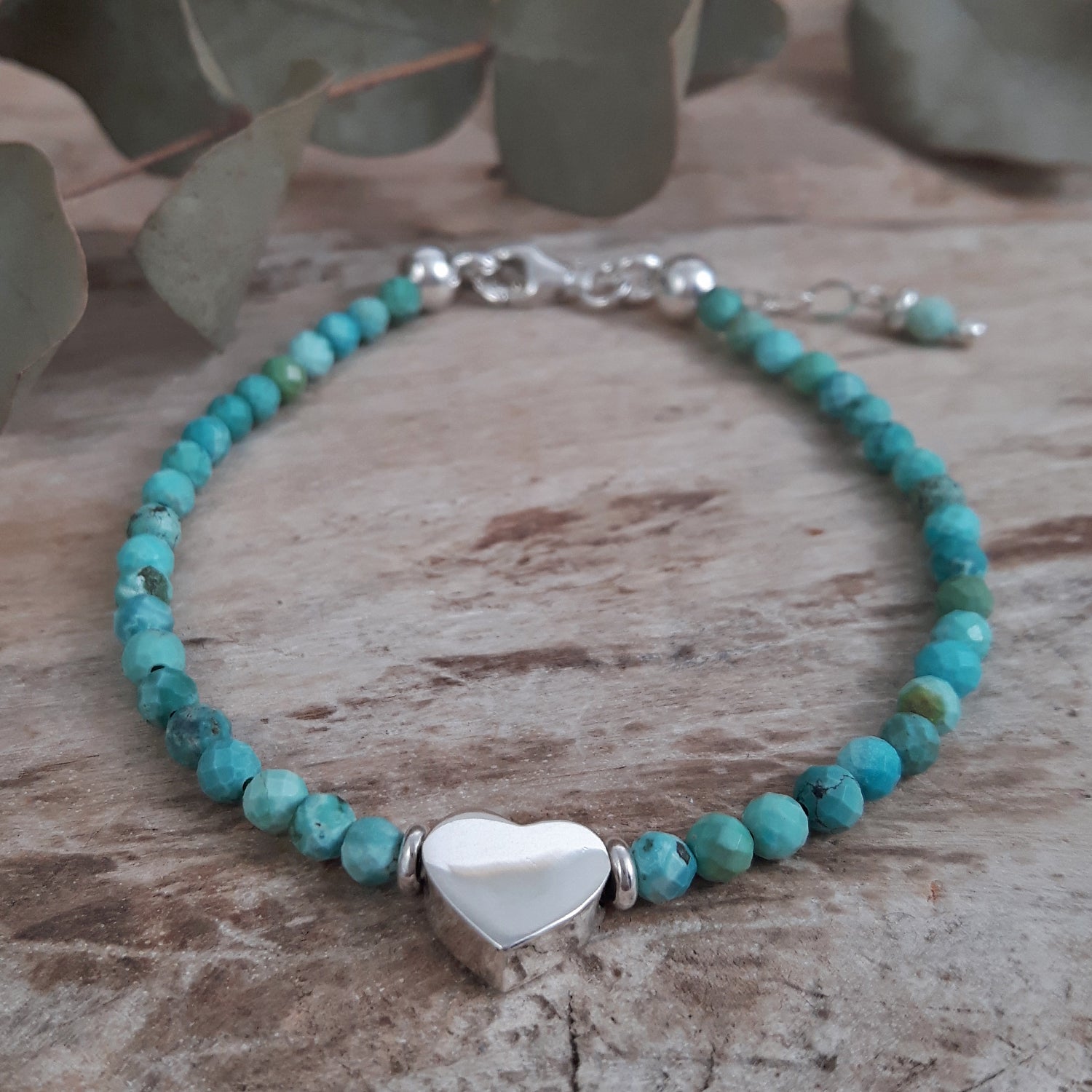 Turquoise gemstone beaded birthstone bracelet with a sterling silver heart charm on a wooden surface.