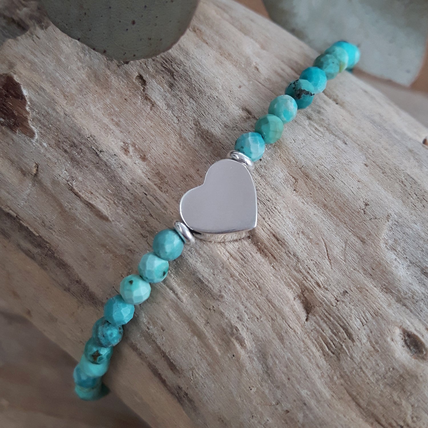 Turquoise gemstone beaded bracelet with a sterling silver heart charm on a wooden surface