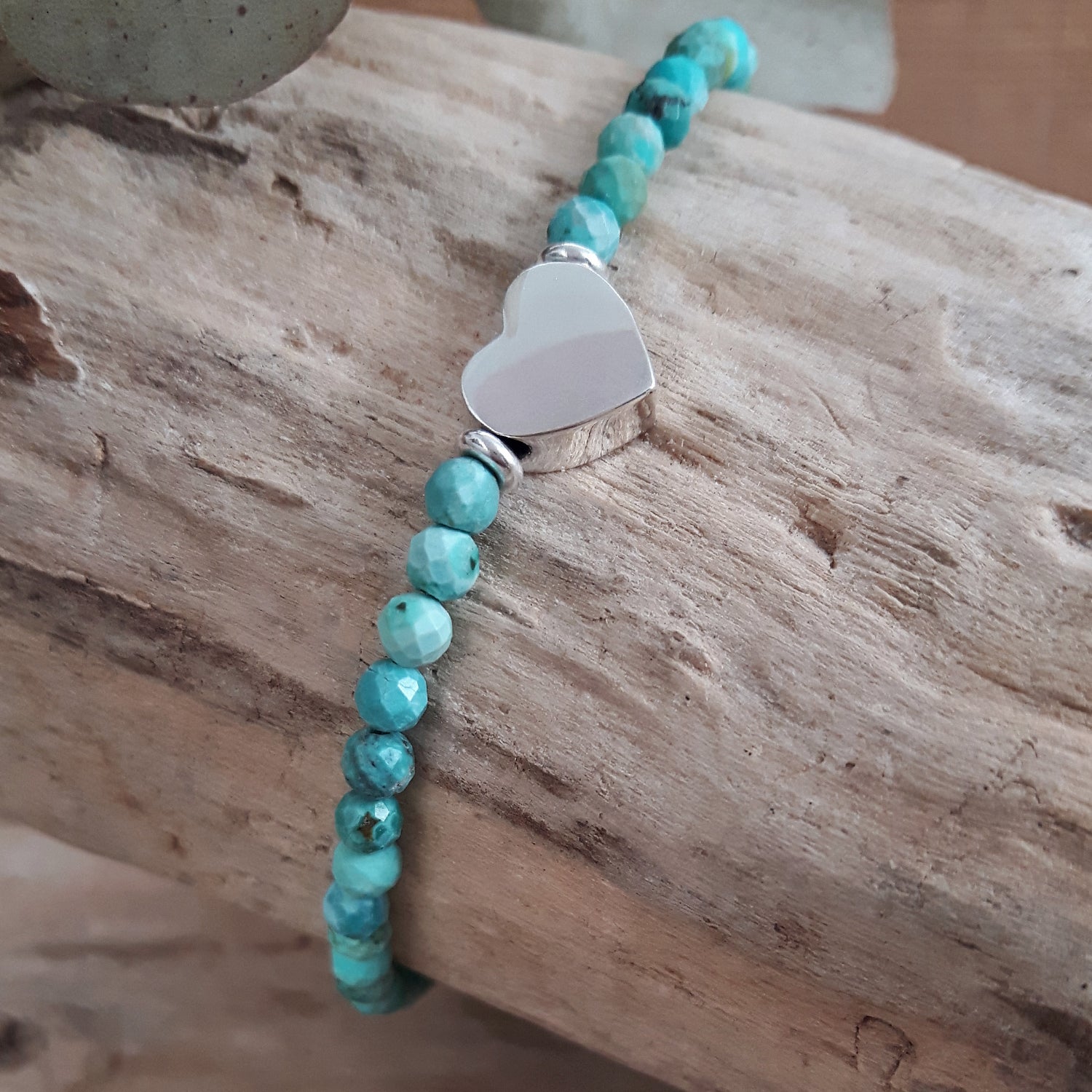 Turquoise beaded birthstone bracelet with a sterling silver heart charm on a wooden surface
