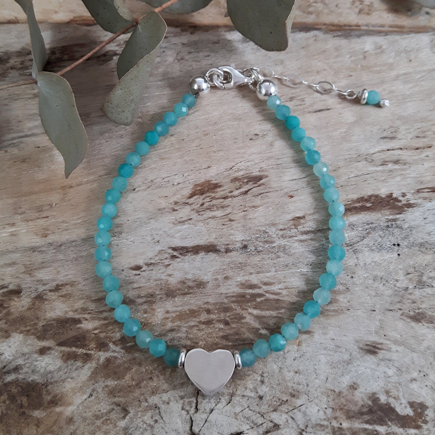 Amazonite beaded bracelet with a sterling silver heart charm on a wooden surface.