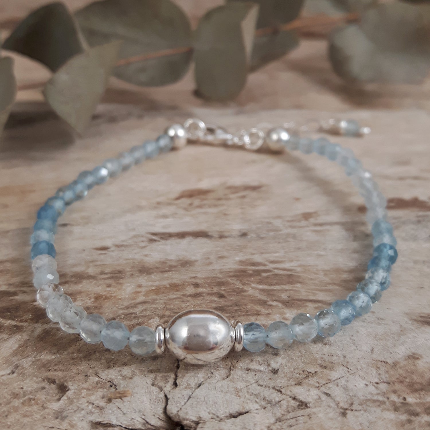 Aquamarine beaded bracelet with sterling silver accents on a wooden surface with green leaves in the background