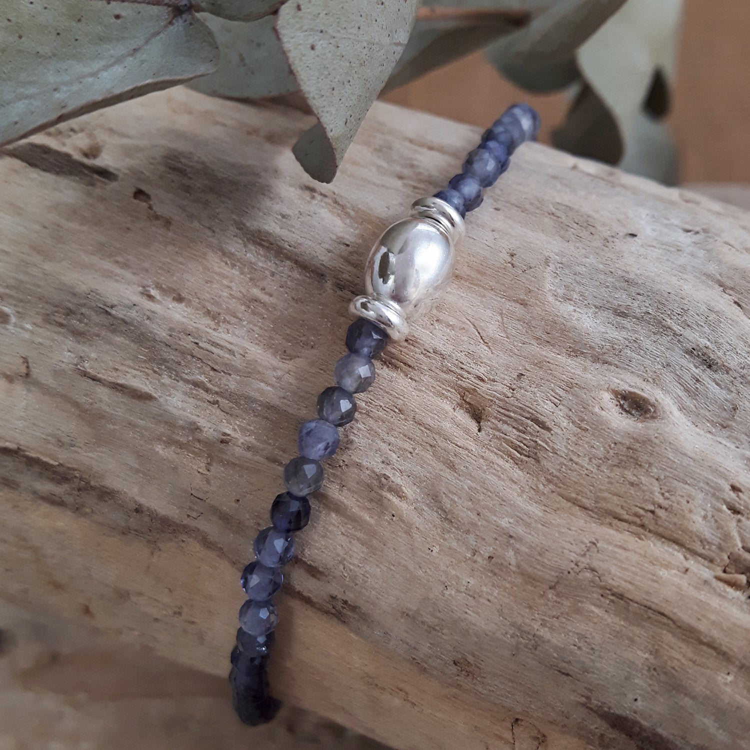 Birthstone bracelet with iolite gemstone beads and a silver bead on a wooden surface with leaves in the background