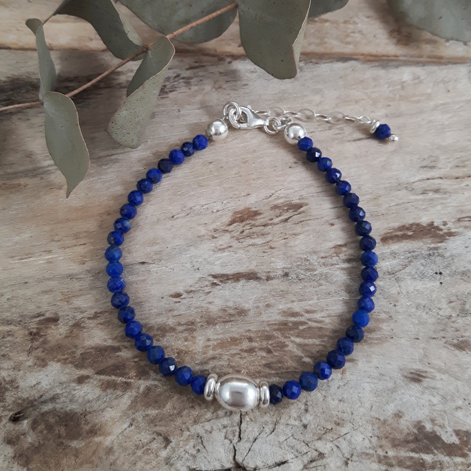 Blue lapis gemstone beaded birthstone bracelet with sterling silver accents on a wooden surface