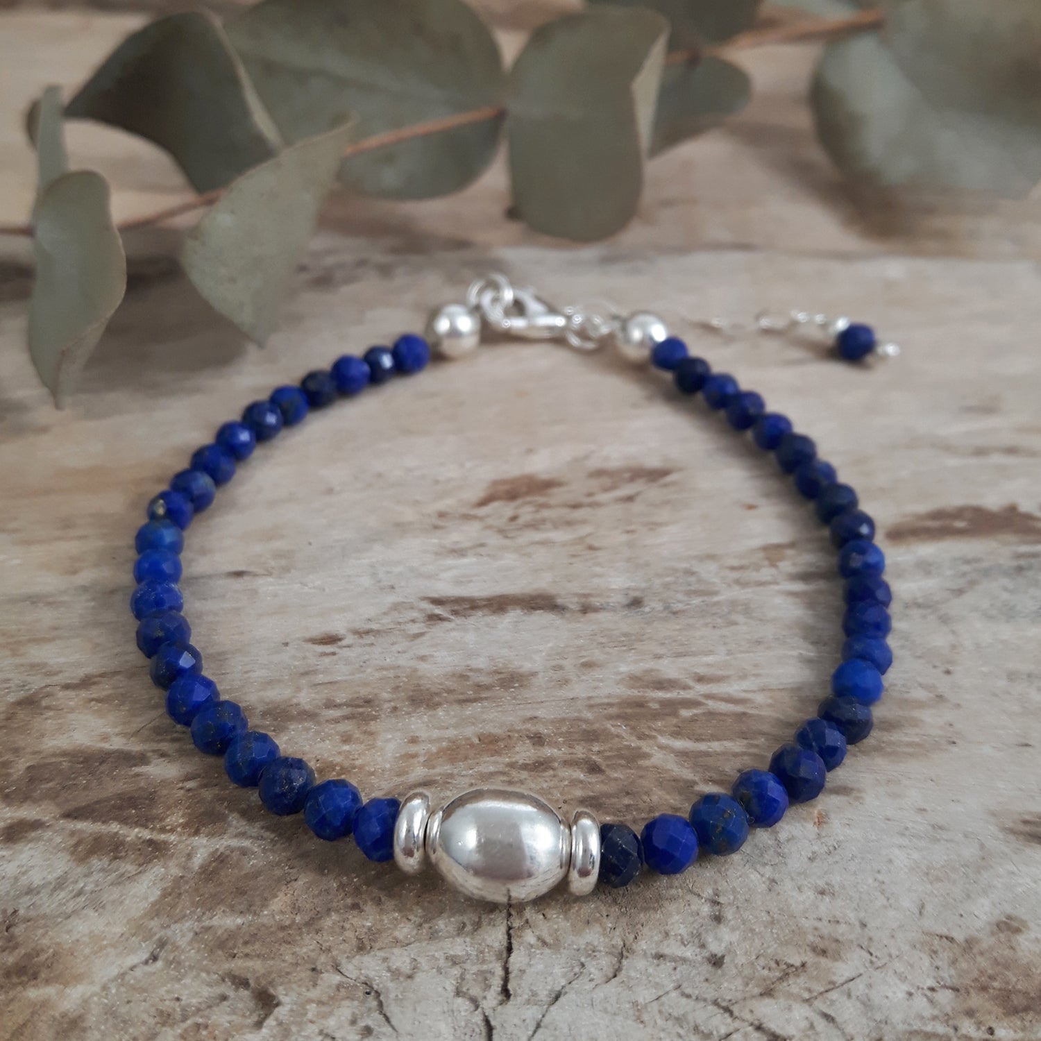 Blue lapis beaded bracelet with sterling silver accents on a wooden surface with leaves in the background