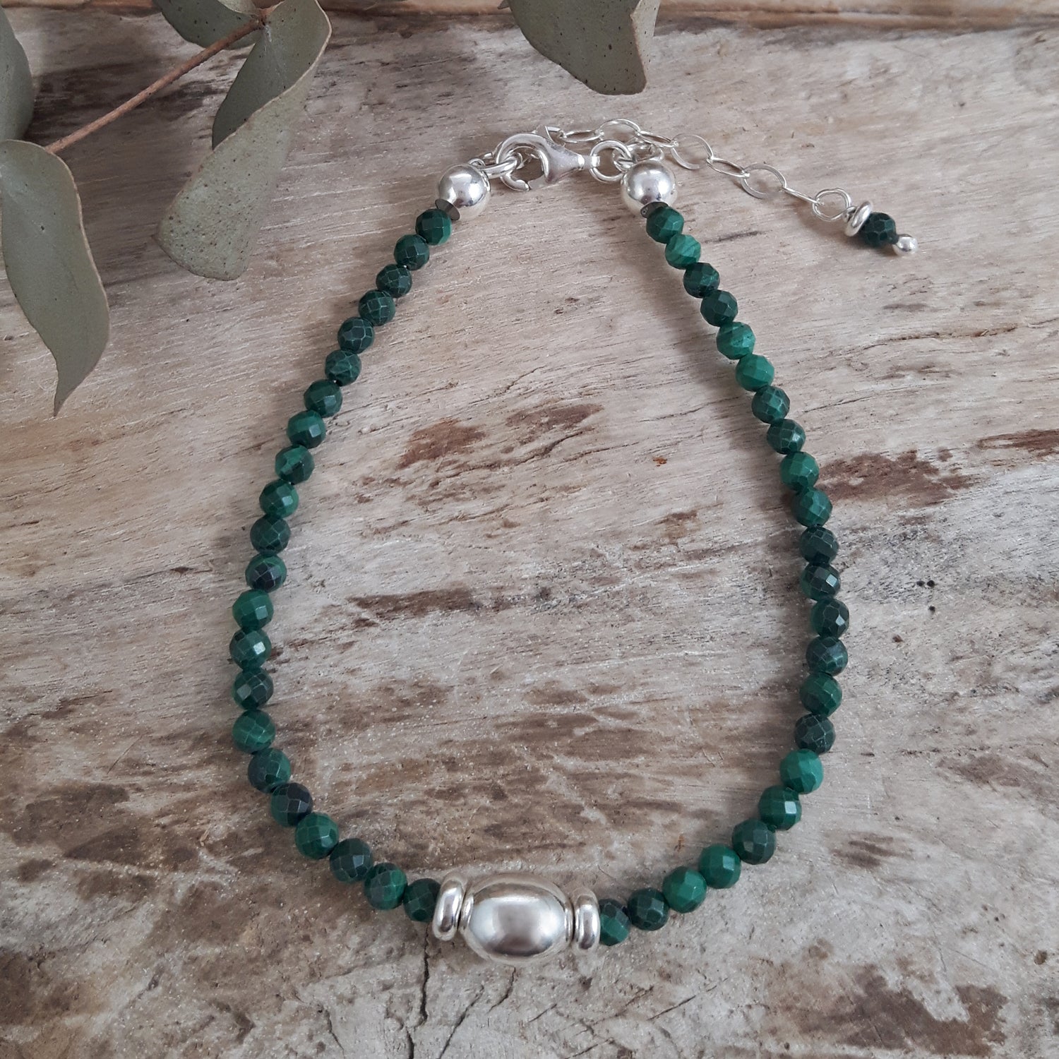 Malchite beaded birthstone bracelet with sterling silver clasp on a wooden surface