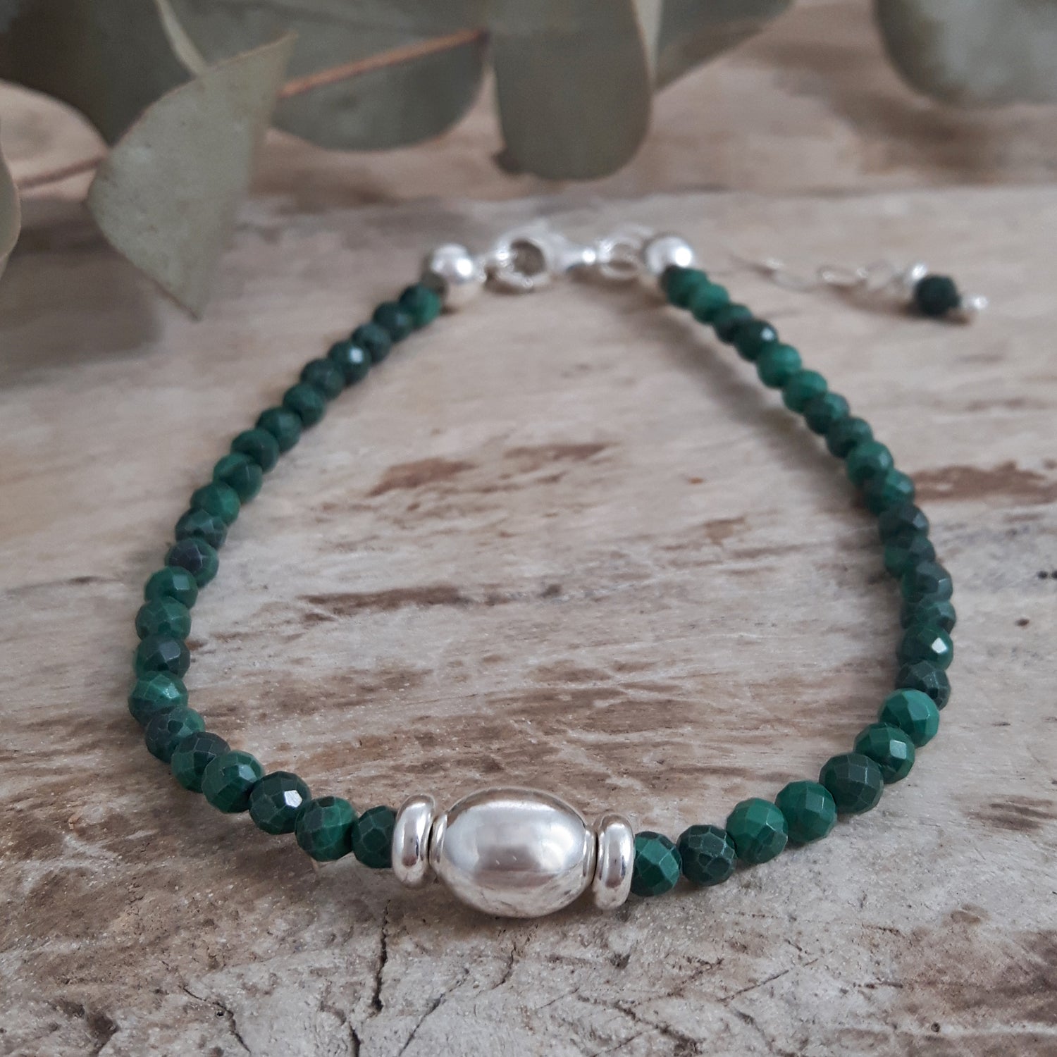 Malachite beaded birthstone bracelet with sterling silver accents on a wooden surface