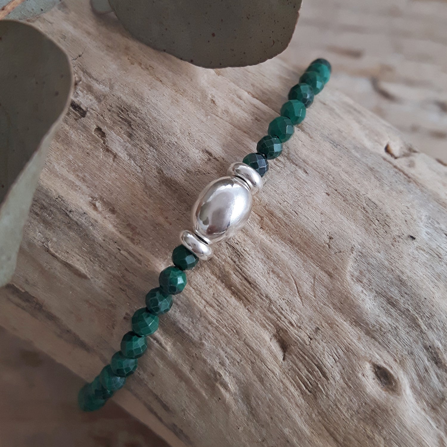 Malachite beaded birthstone bracelet with a sterling silver detail on a wooden surface