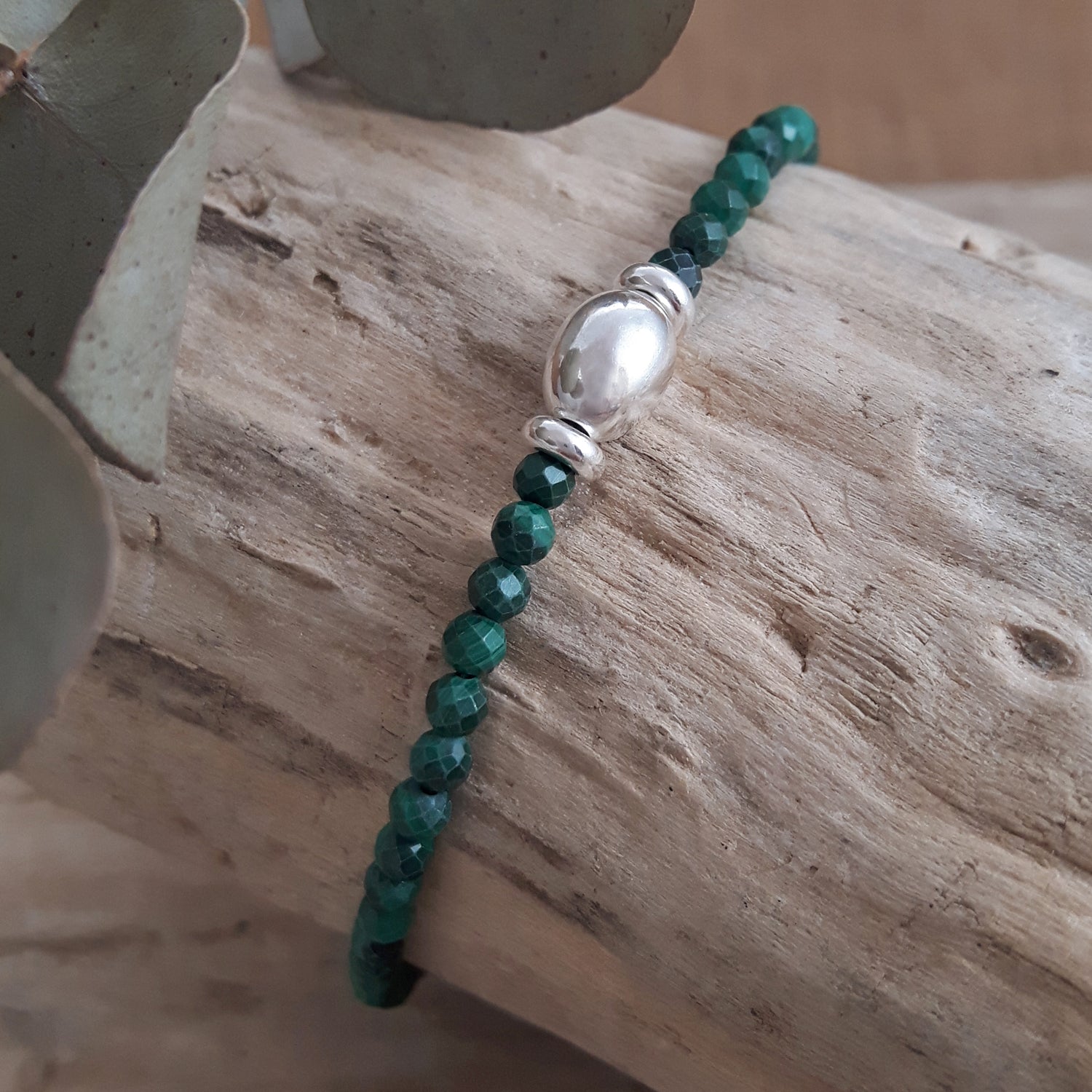 Malachite beaded birthstone bracelet with a sterling silver clasp on a wooden surface