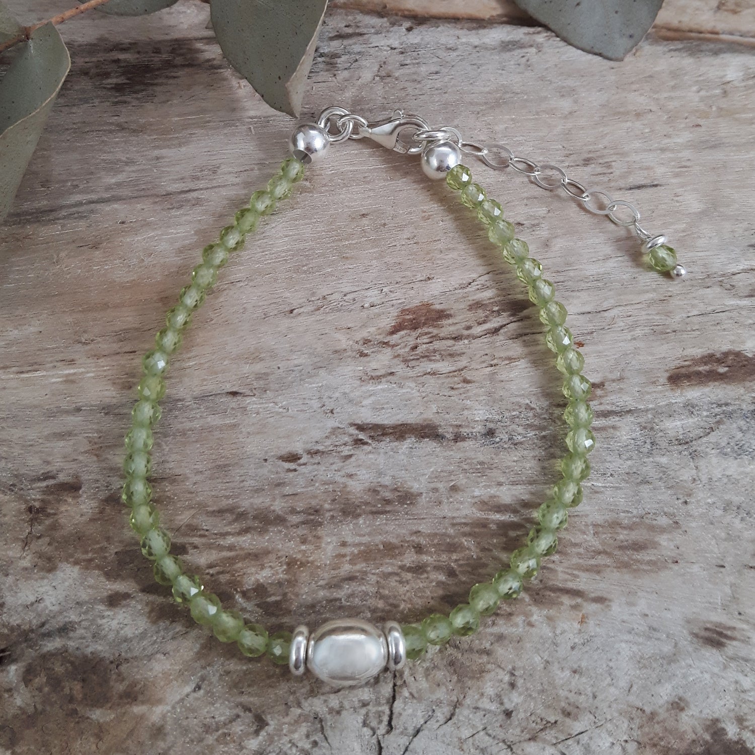Green peridot gemstone beaded bracelet with sterling silver bead detail on a wooden surface