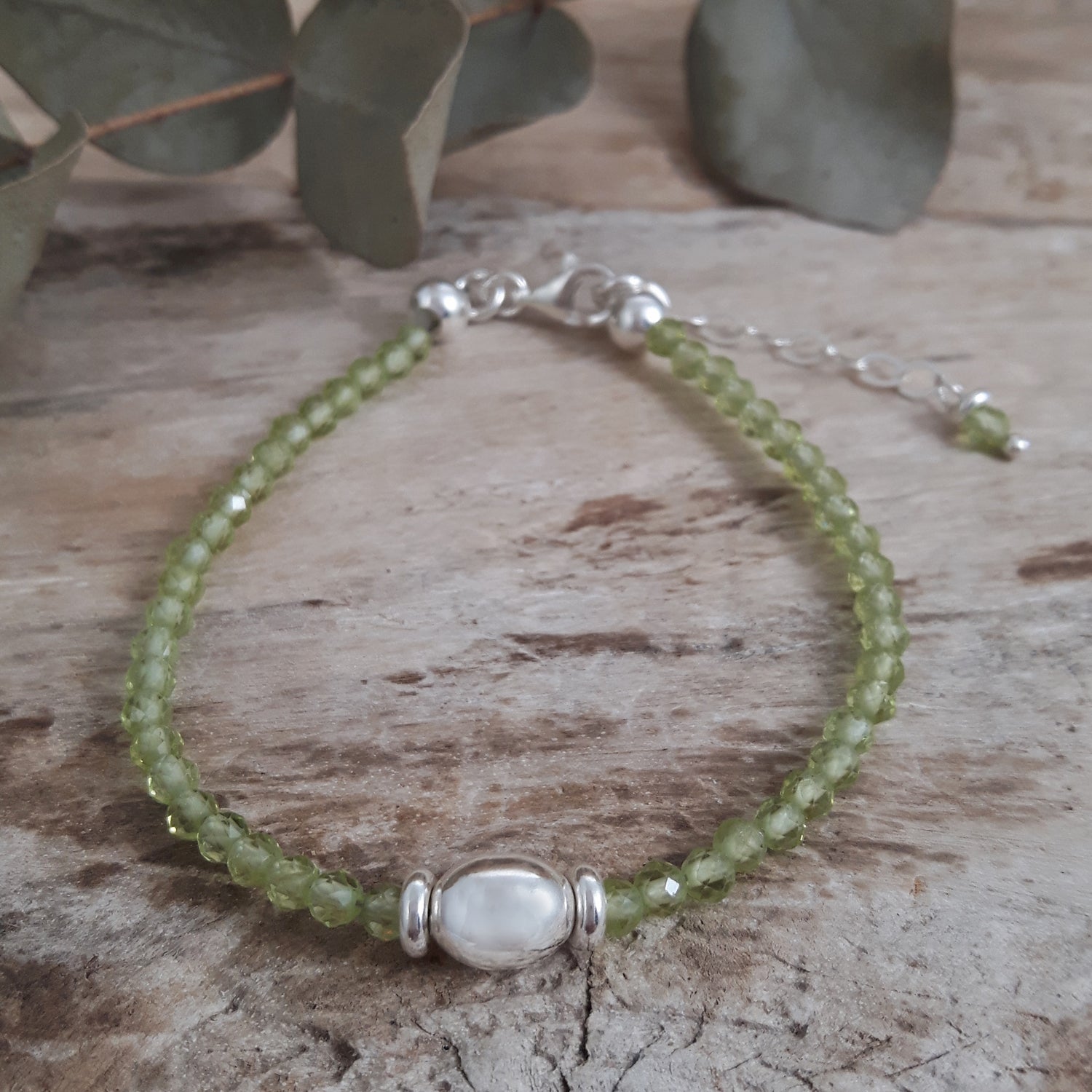 Green Peridot beaded bracelet with sterling silver bead detail on a wooden surface with eucalyptus leaves.