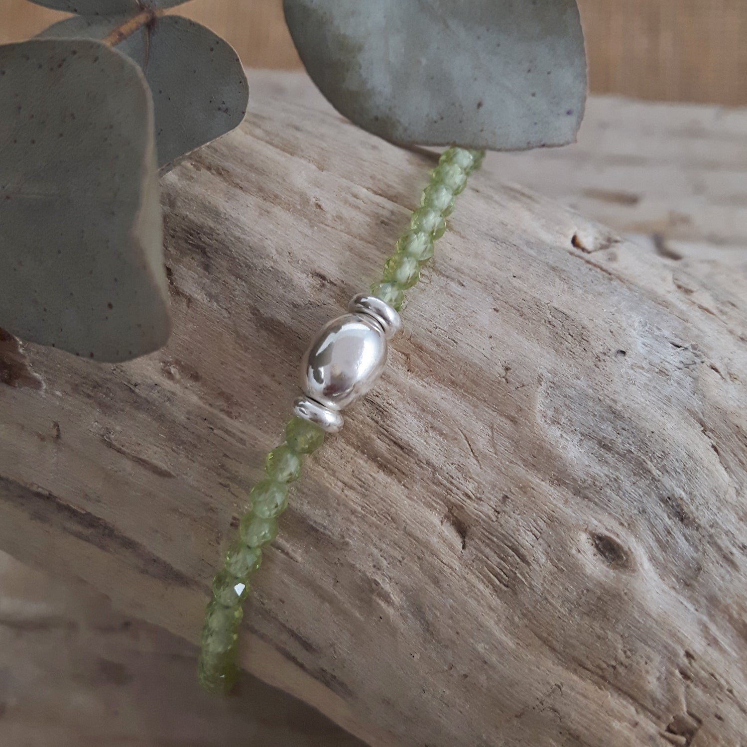 Green Peridot birthstone beaded bracelet with a sterling silver bead on a wooden surface
