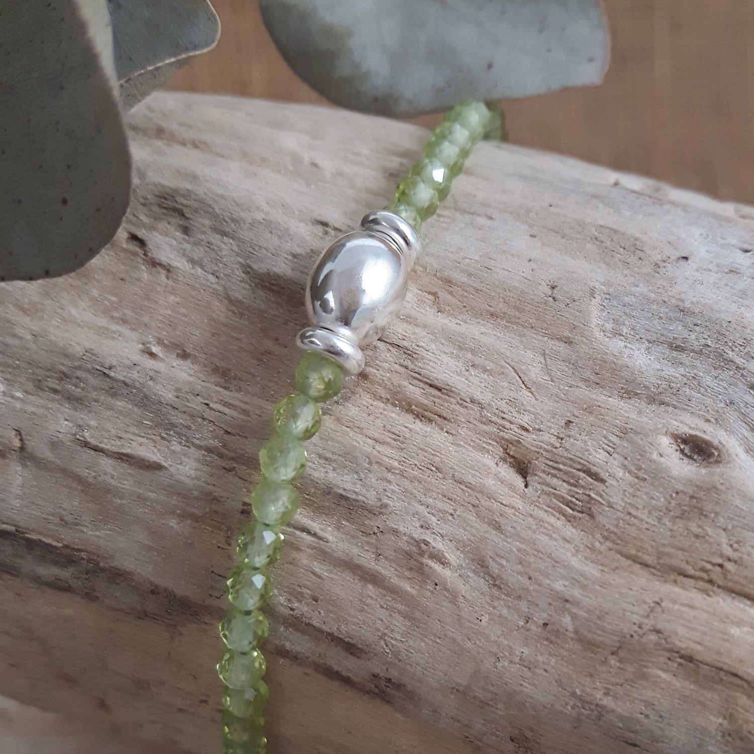 Green Peridot gemstone beaded bracelet with a sterling silver orb bead on a wooden surface