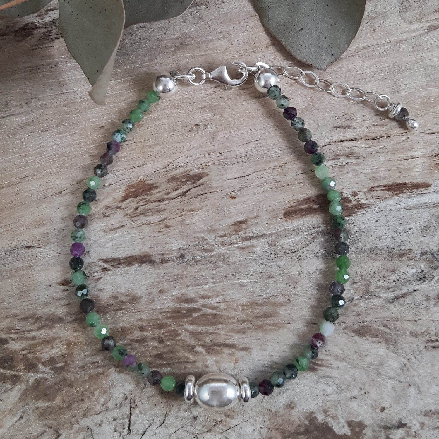 Gemstone July birthstone beaded bracelet with green and purple stones on a wooden surface