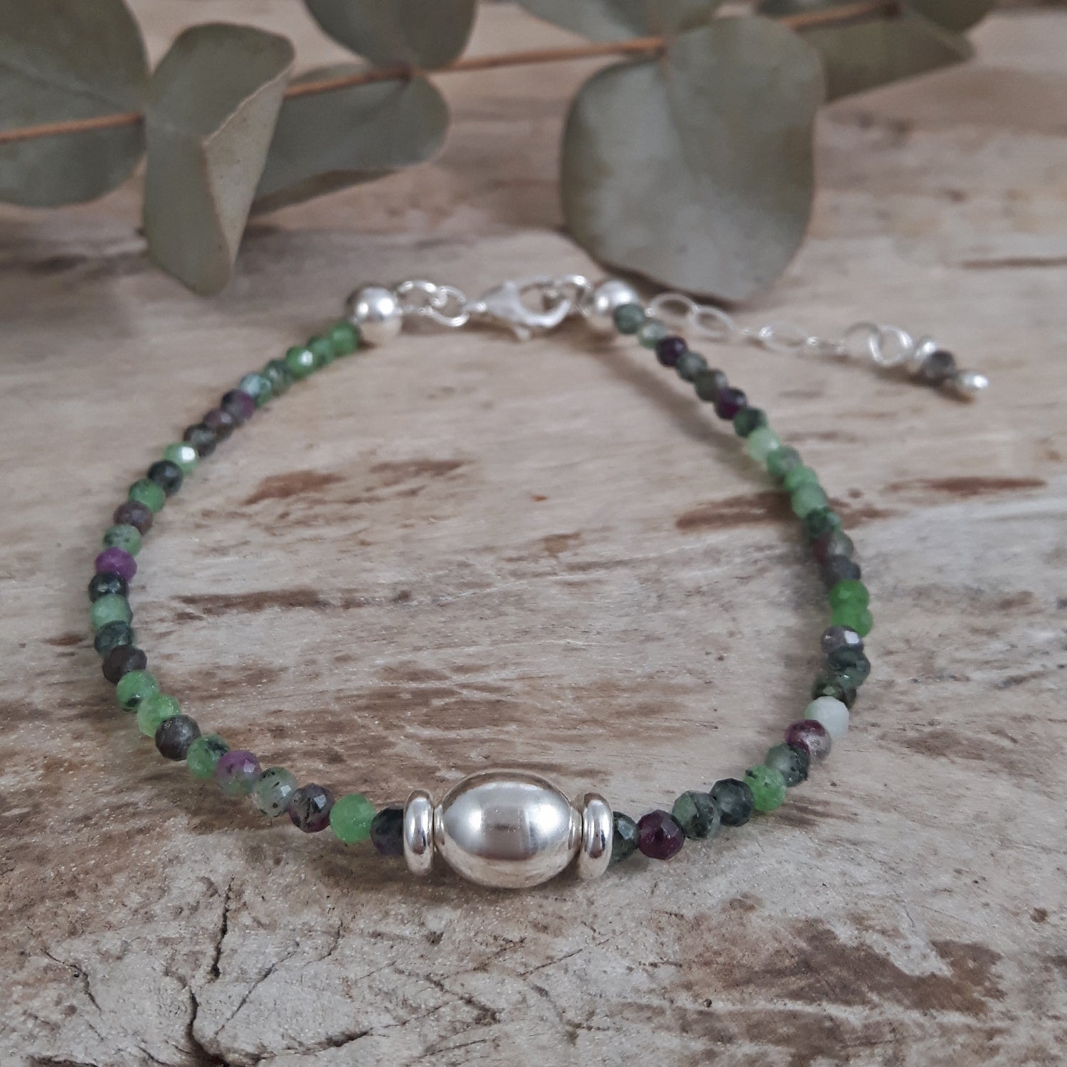 Ruby Zoisite beaded bracelet with green and purple stones on a wooden surface with eucalyptus leaves.