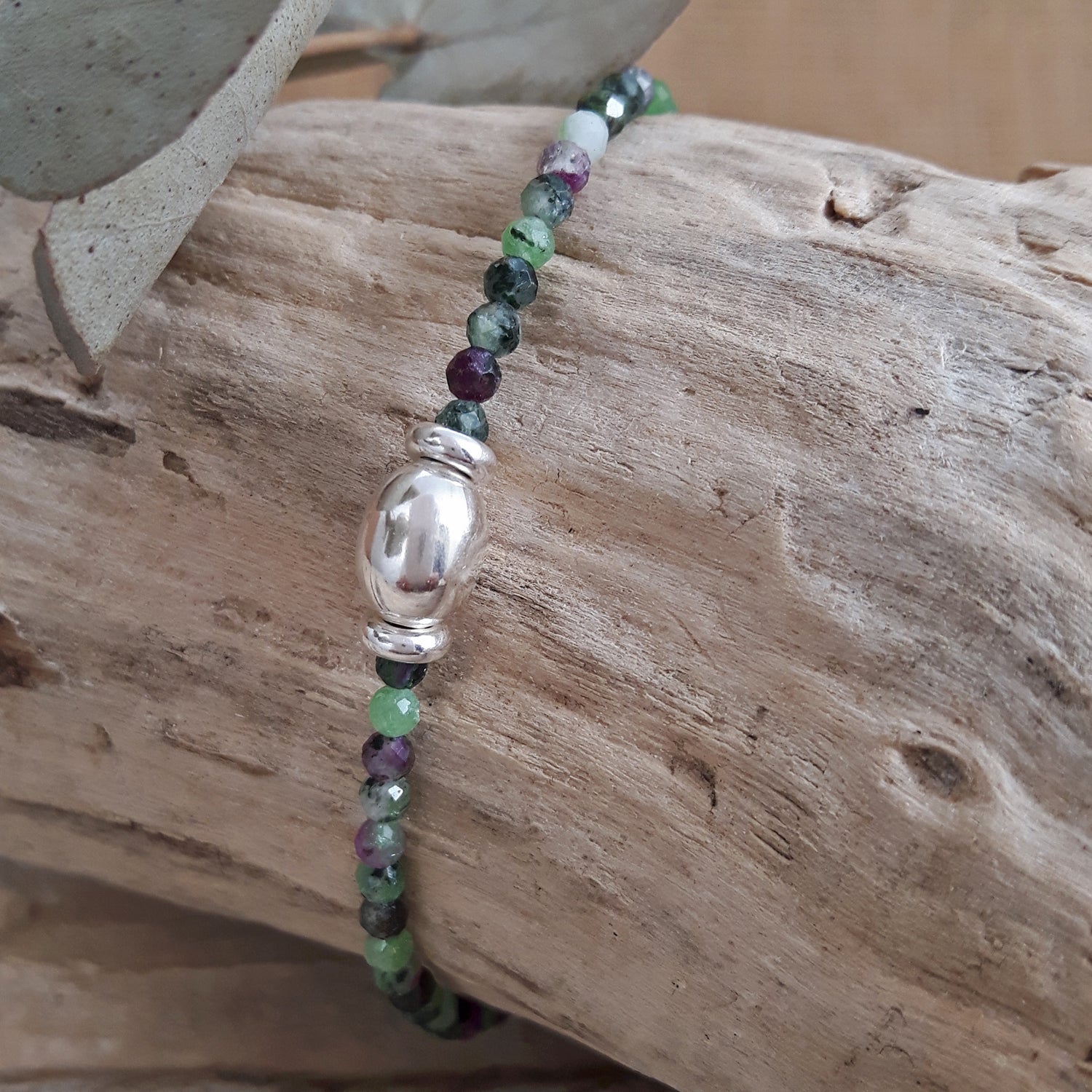 Ruby Zoisite Birthstone Beaded bracelet with a silver bead on a wooden surface