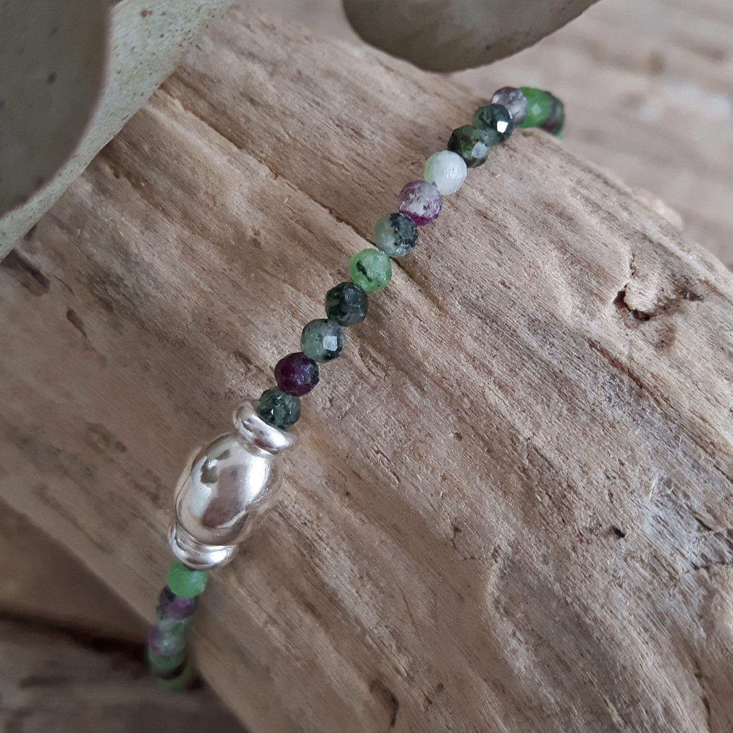 Gemstone beaded bracelet with a sterling silver bead on a wooden surface