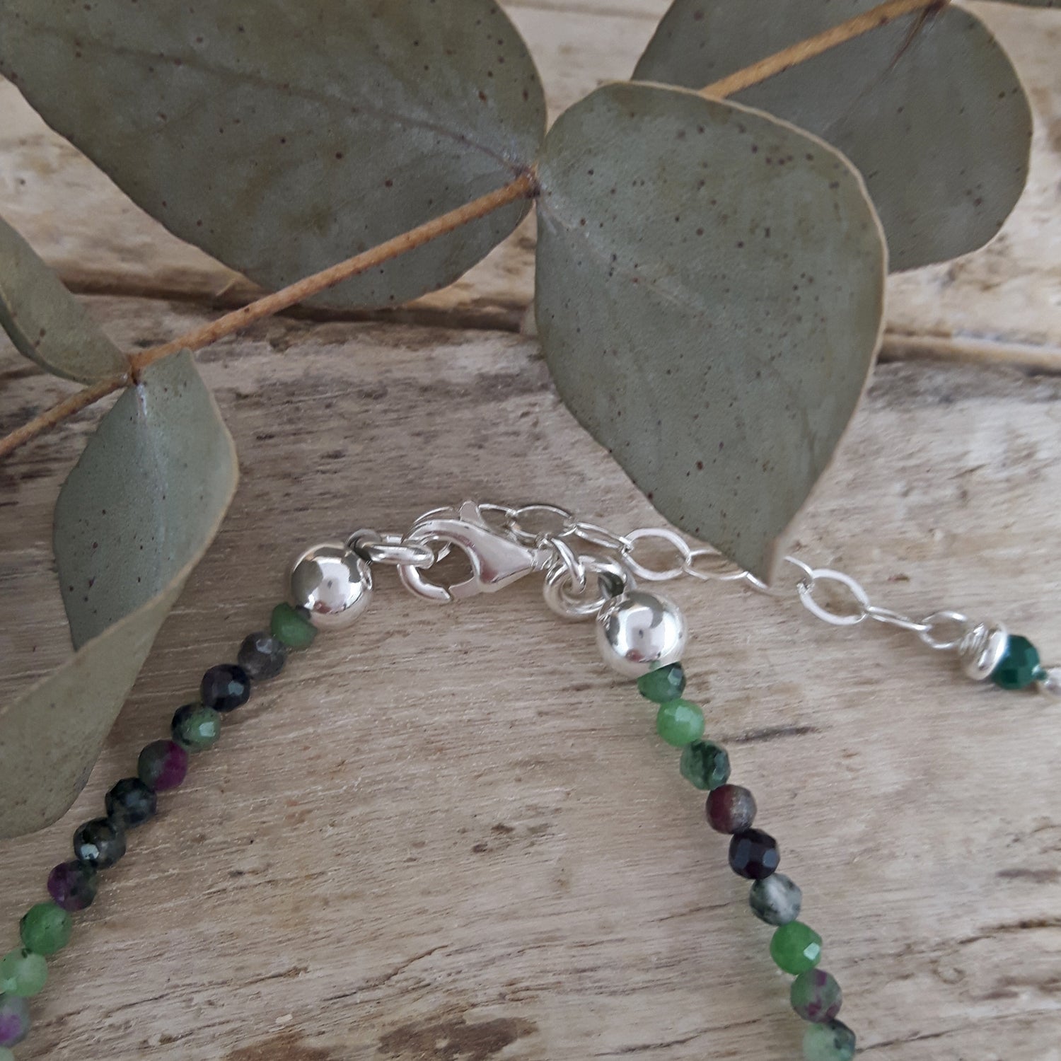 Sterling silver birthstone bracelet with Ruby Zoisite beads on a wooden surface with eucalyptus leaves