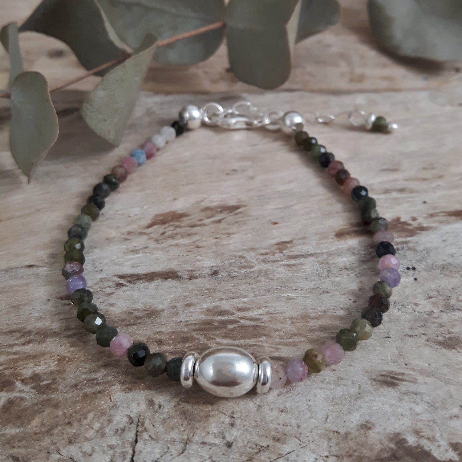 Tourmaline beaded birthstone bracelet with sterling silver detail on a wooden surface with eucalyptus leaves.