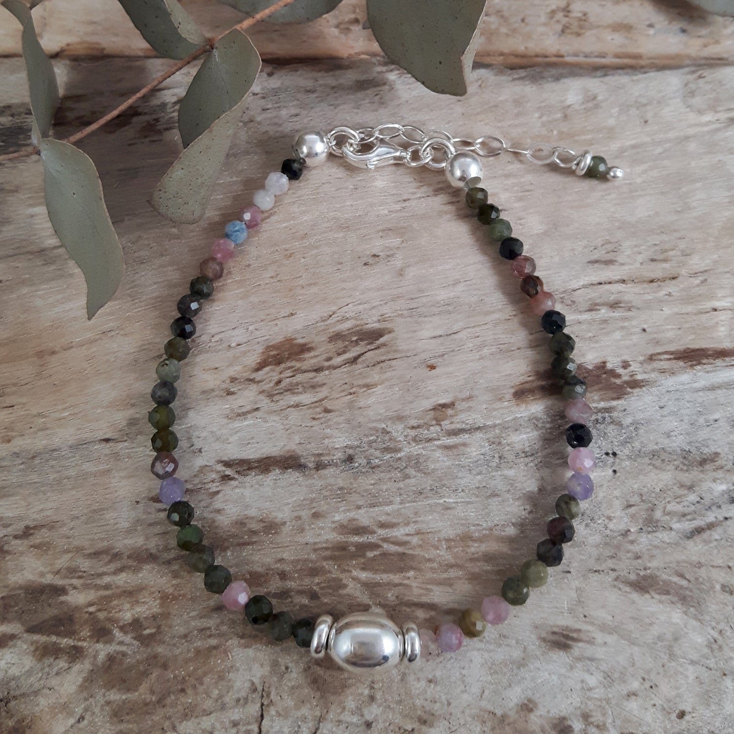 Beaded tourmaline birthstone bracelet with sterling silver bead on a wooden surface