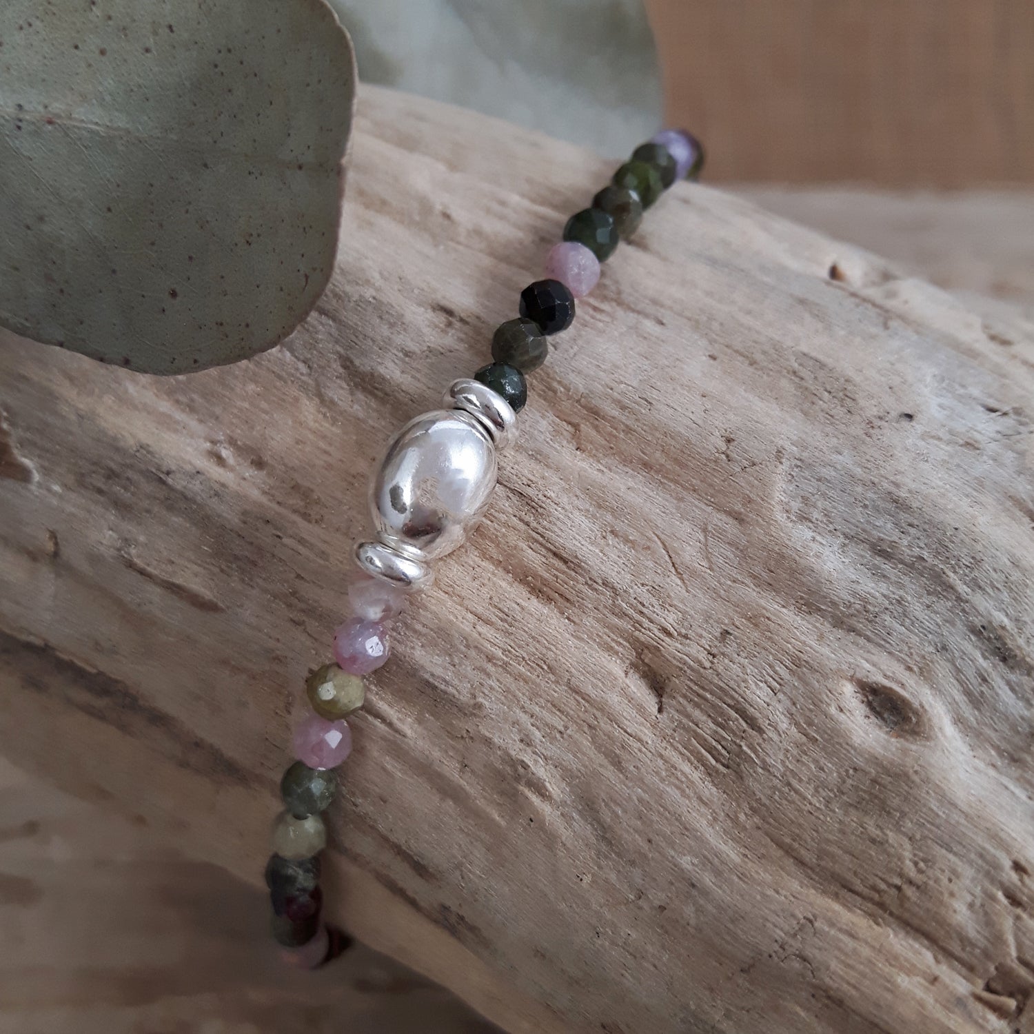 Birthstone bracelet with multicoloured tourmaline gemstone beads and a sterling silver bead on a wooden surface