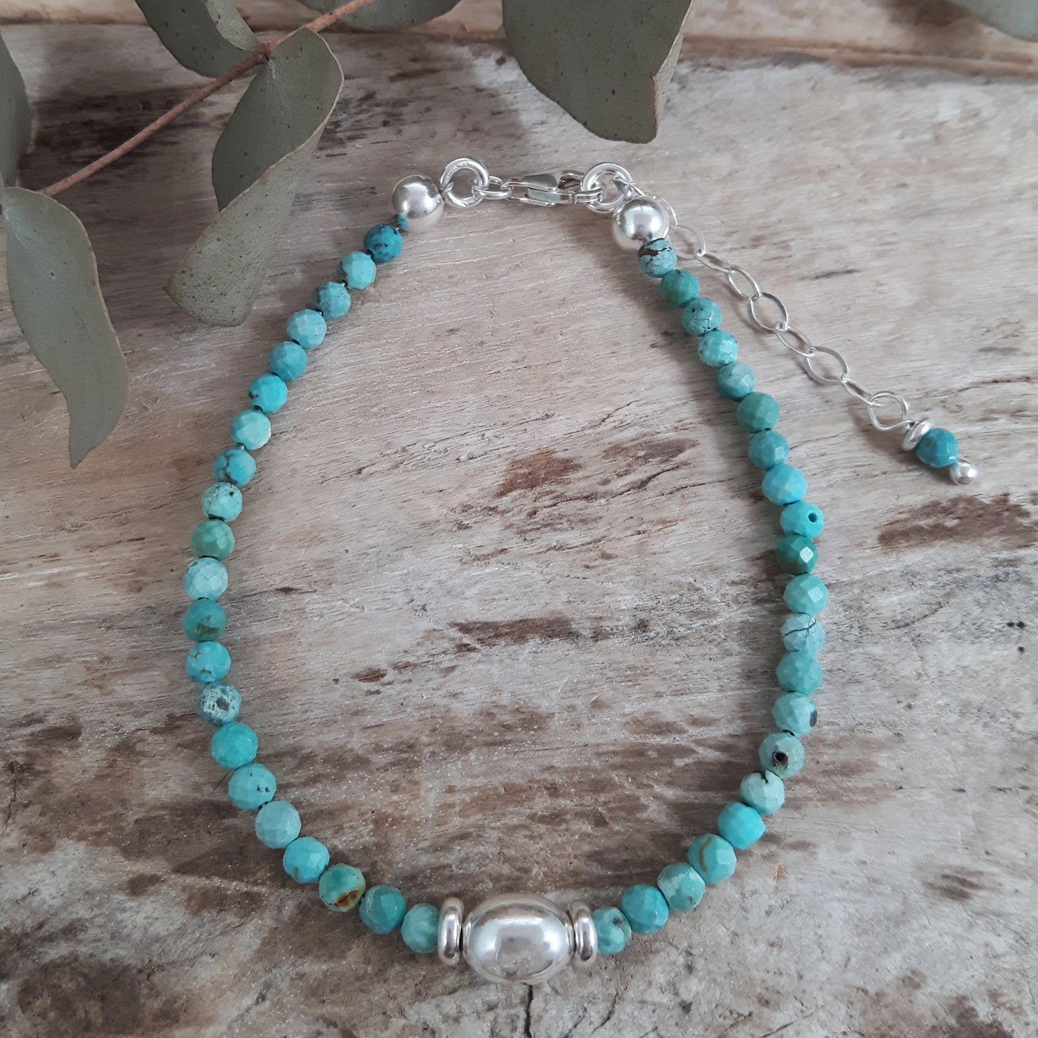 Turquoise gemstone beaded birthstone bracelet with a sterling silver orb bead on a wooden surface