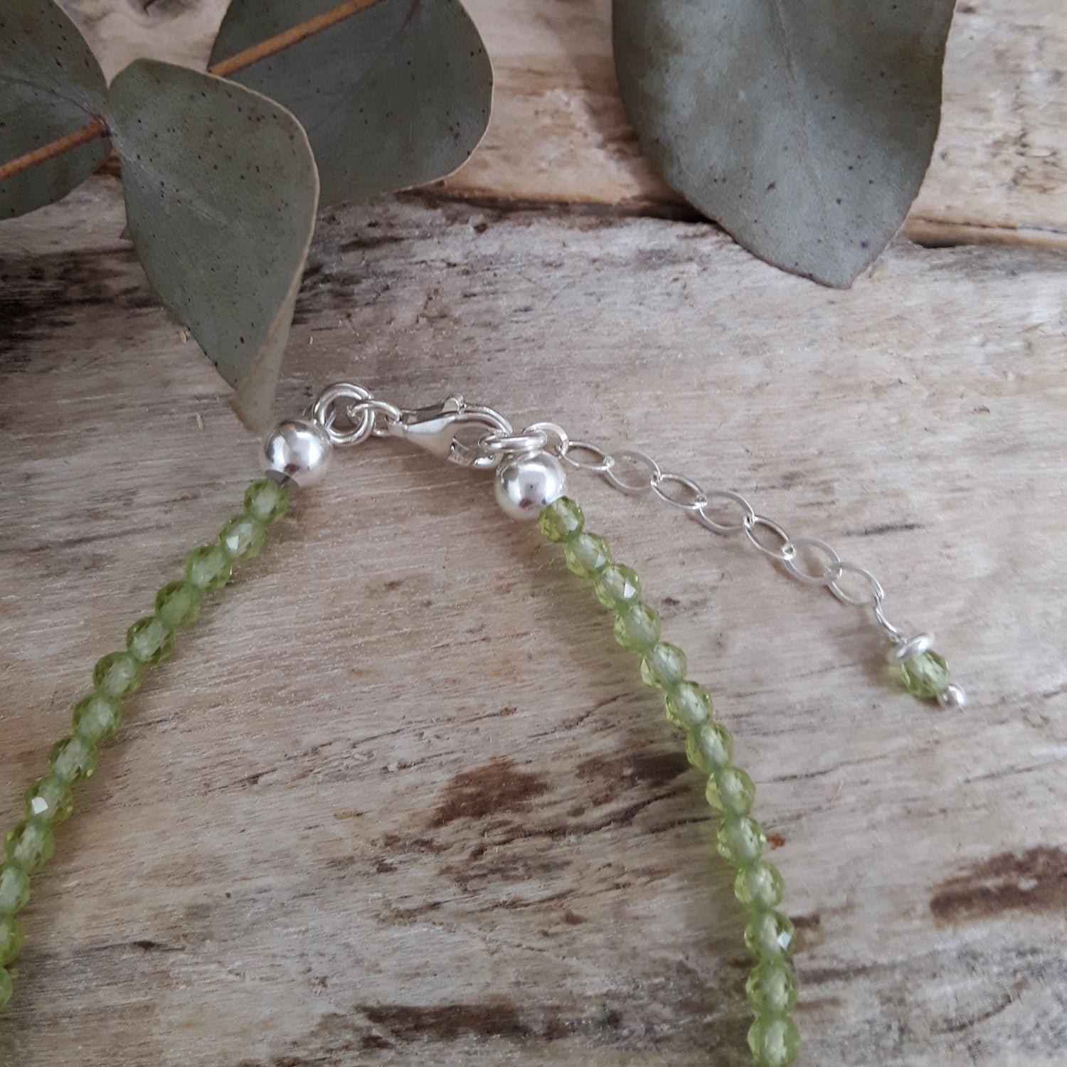 Green peridot beaded birthstone bracelet with sterling silver extension chain on a wooden surface