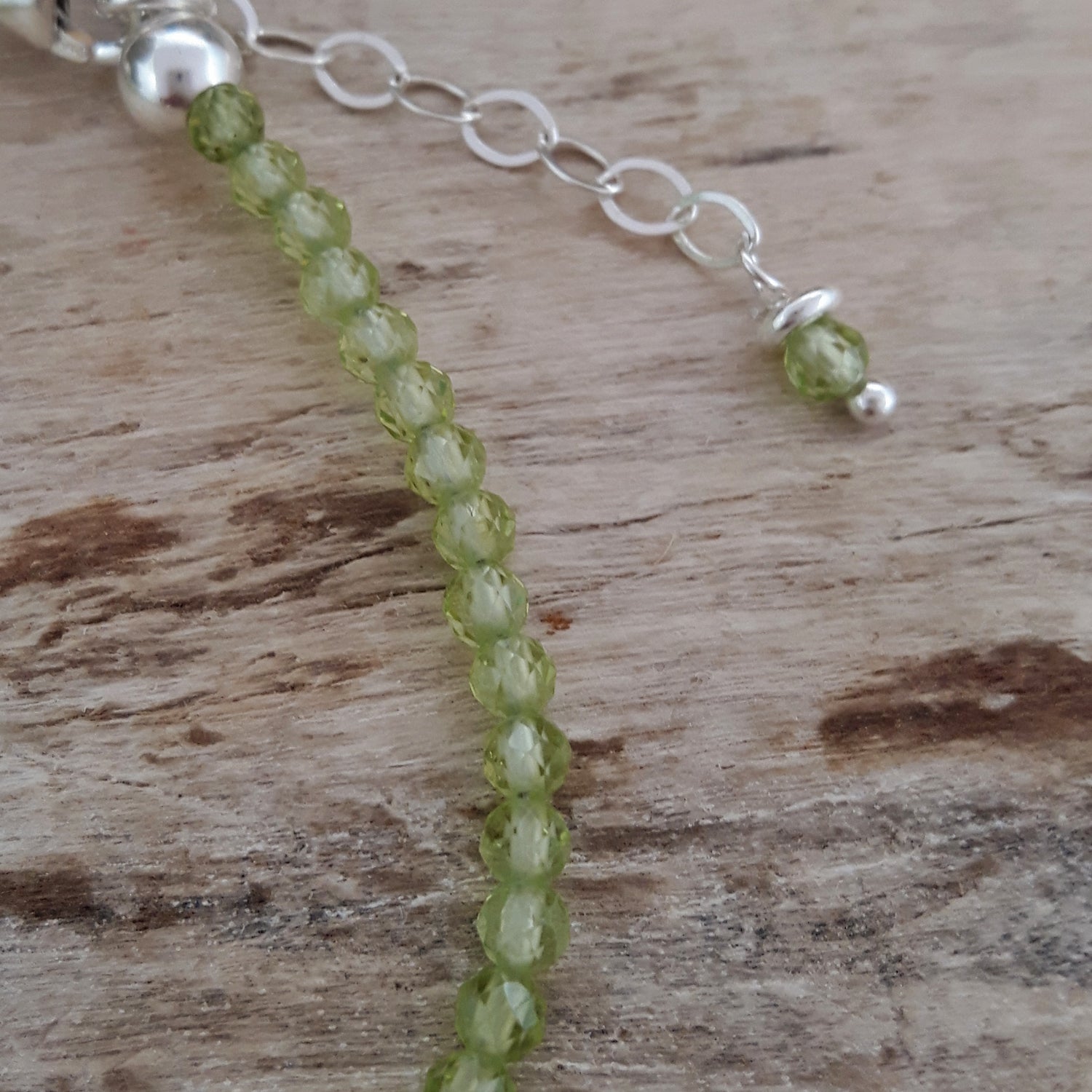 Green peridot gemstone beaded bracelet with sterling silver extender chain on a wooden surface