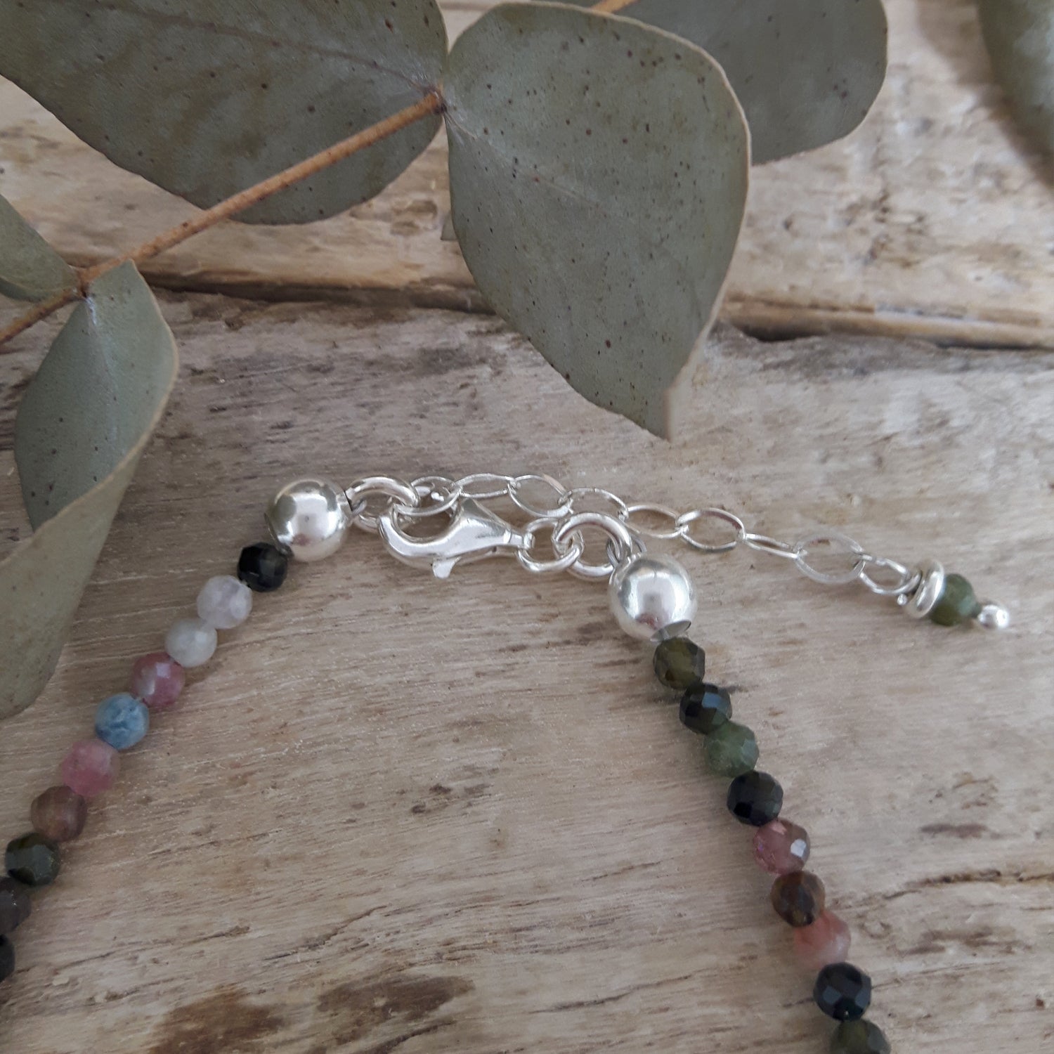 Tourmaline beaded bracelet with sterling silver clasp on a wooden surface with eucalyptus leaves