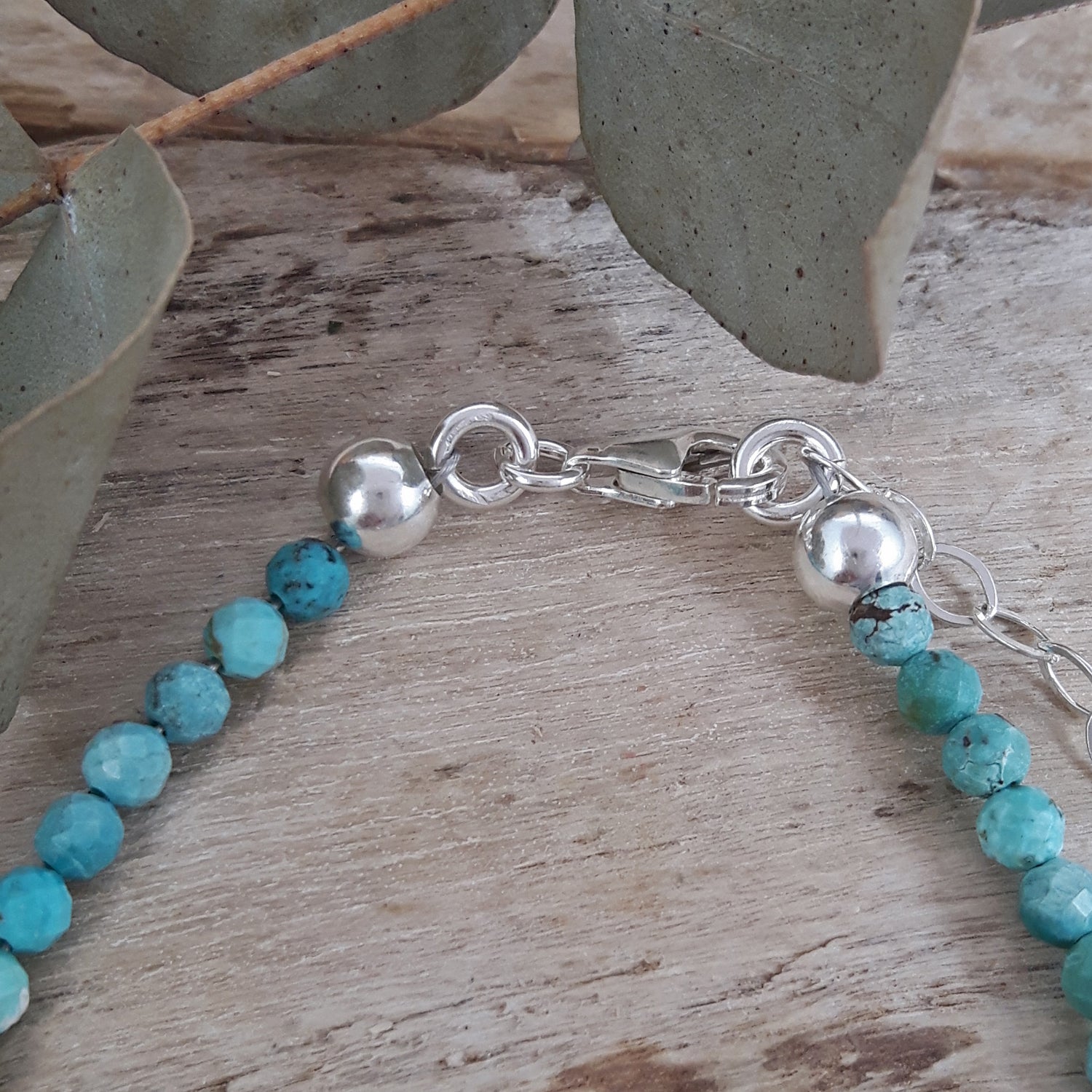 Turquoise gemstone beaded December birthstone bracelet with sterling silver clasp on a wooden surface