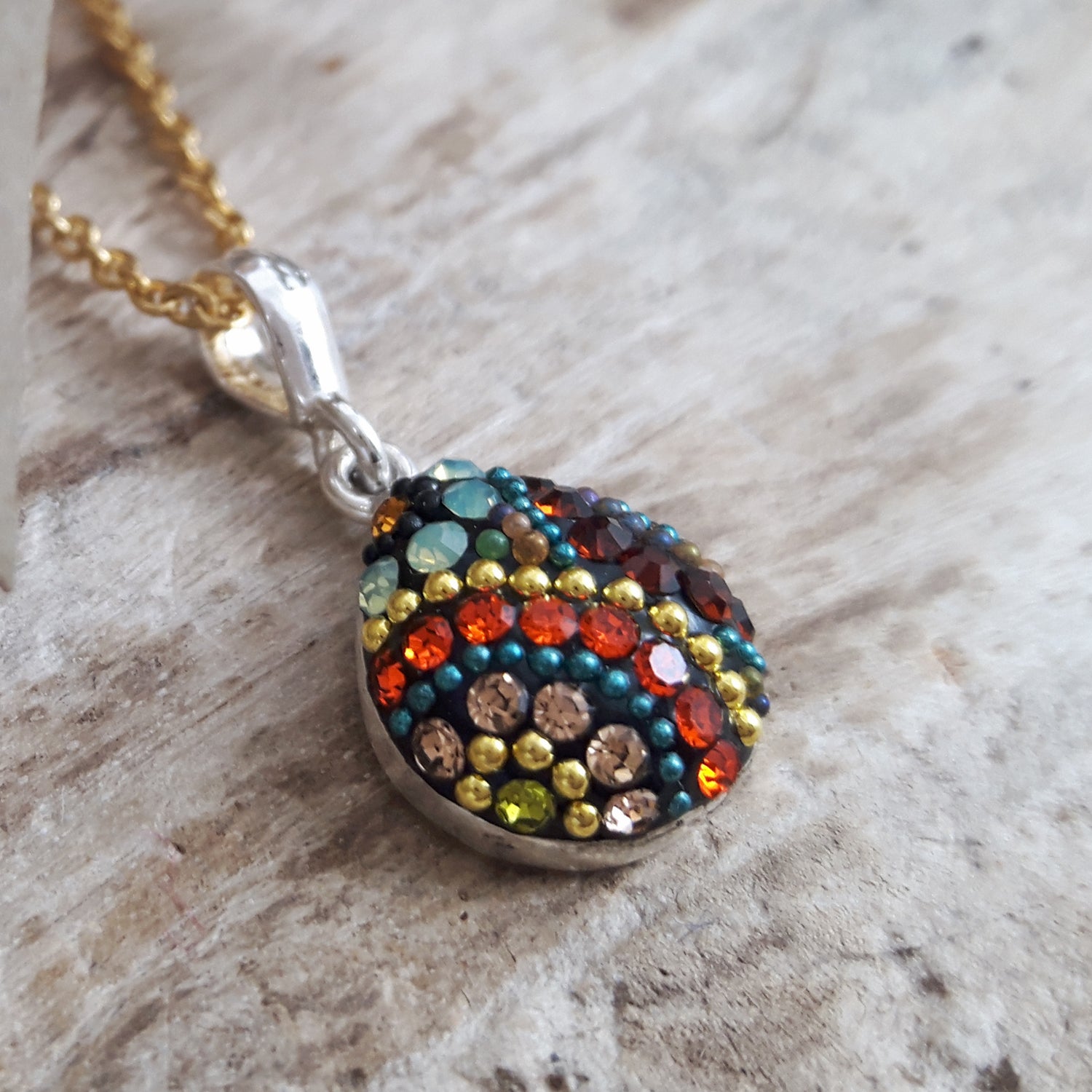Colourful beaded pendant on a gold-plated chain against a wooden background