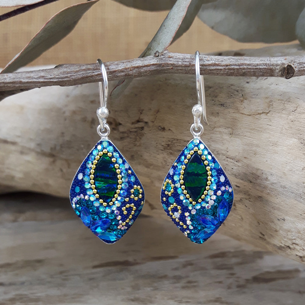 A pair of drop earrings featuring a central emerald-cut gemstone with a frame of encrusted micro-pearls and beads in shades of blue and green, mounted on silver hooks.