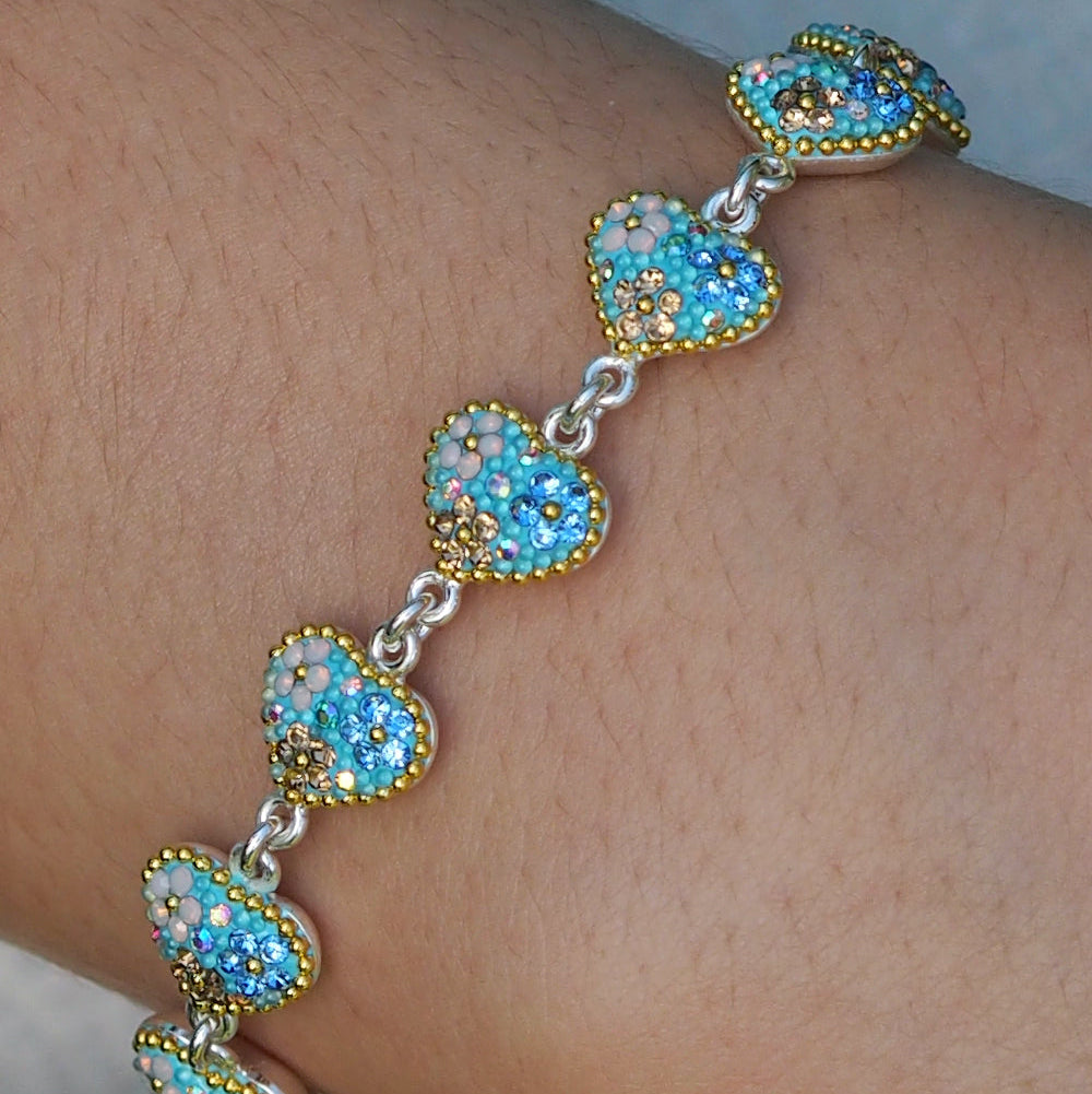A sterling silver bracelet with turquoise, aqua, and gold tones, featuring linked hearts with crystal and micro-bead accents.