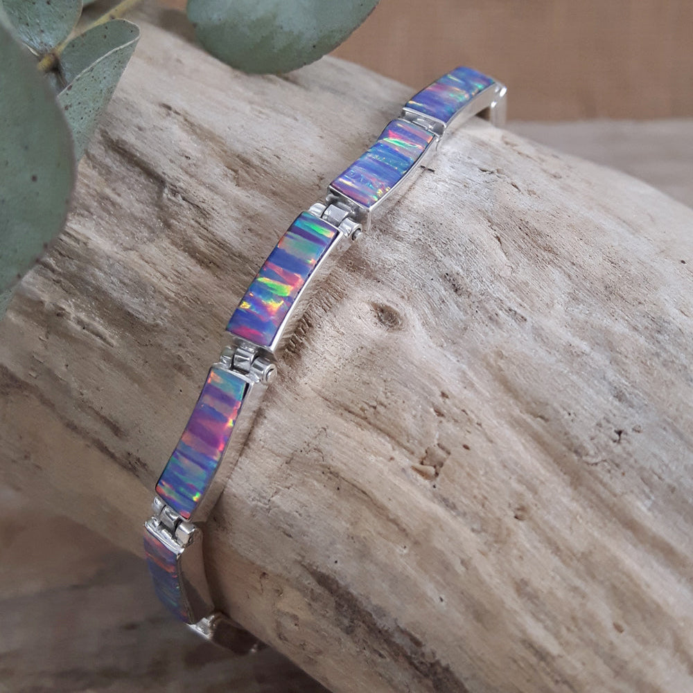 A bracelet with spectral lavender opal stones, framed in sterling silver, displayed on a wooden branch.