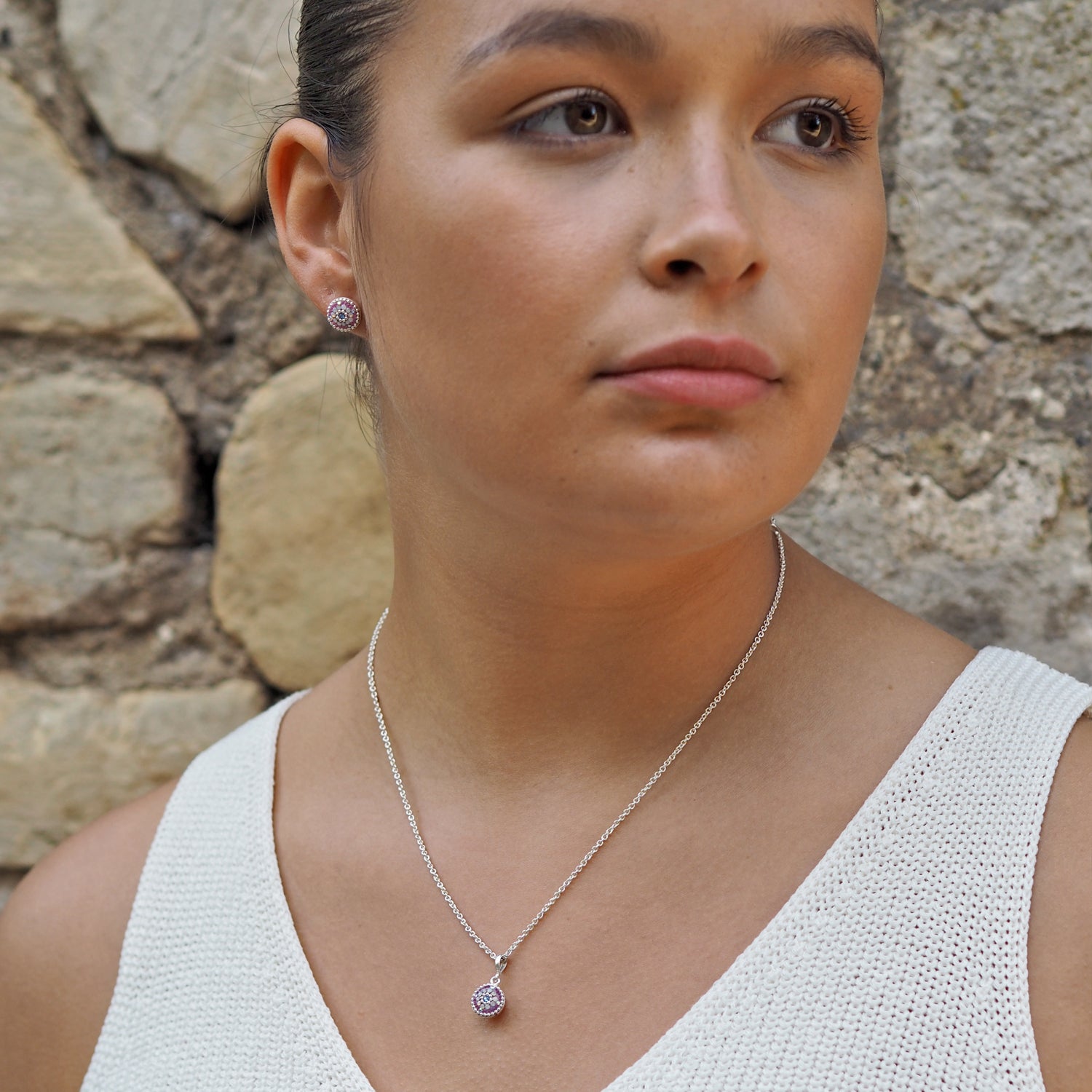 Model wearing a silver necklace with a lilac dream pendant and earrings against a stone wall.