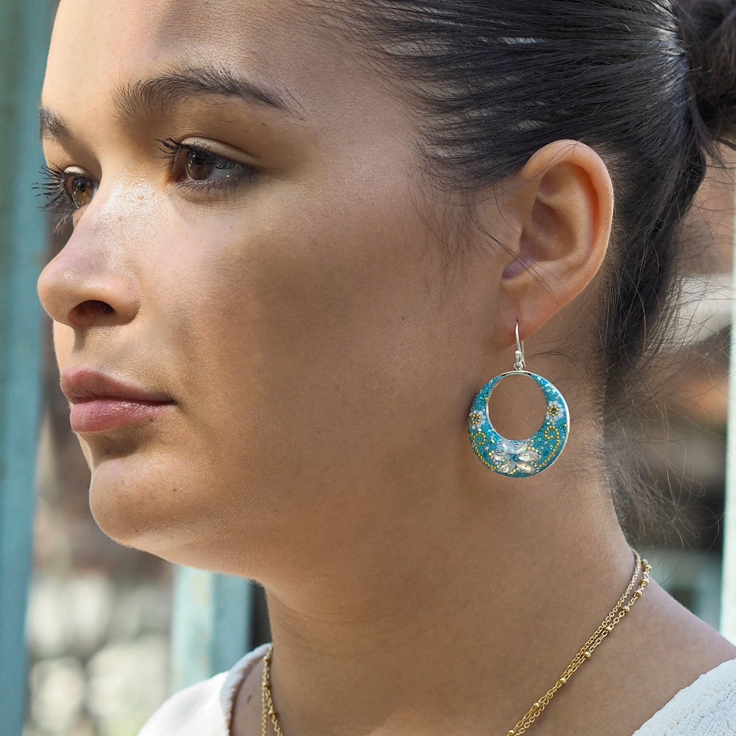 Close-up of a woman wearing a blue floral hoop earring with a blurred background