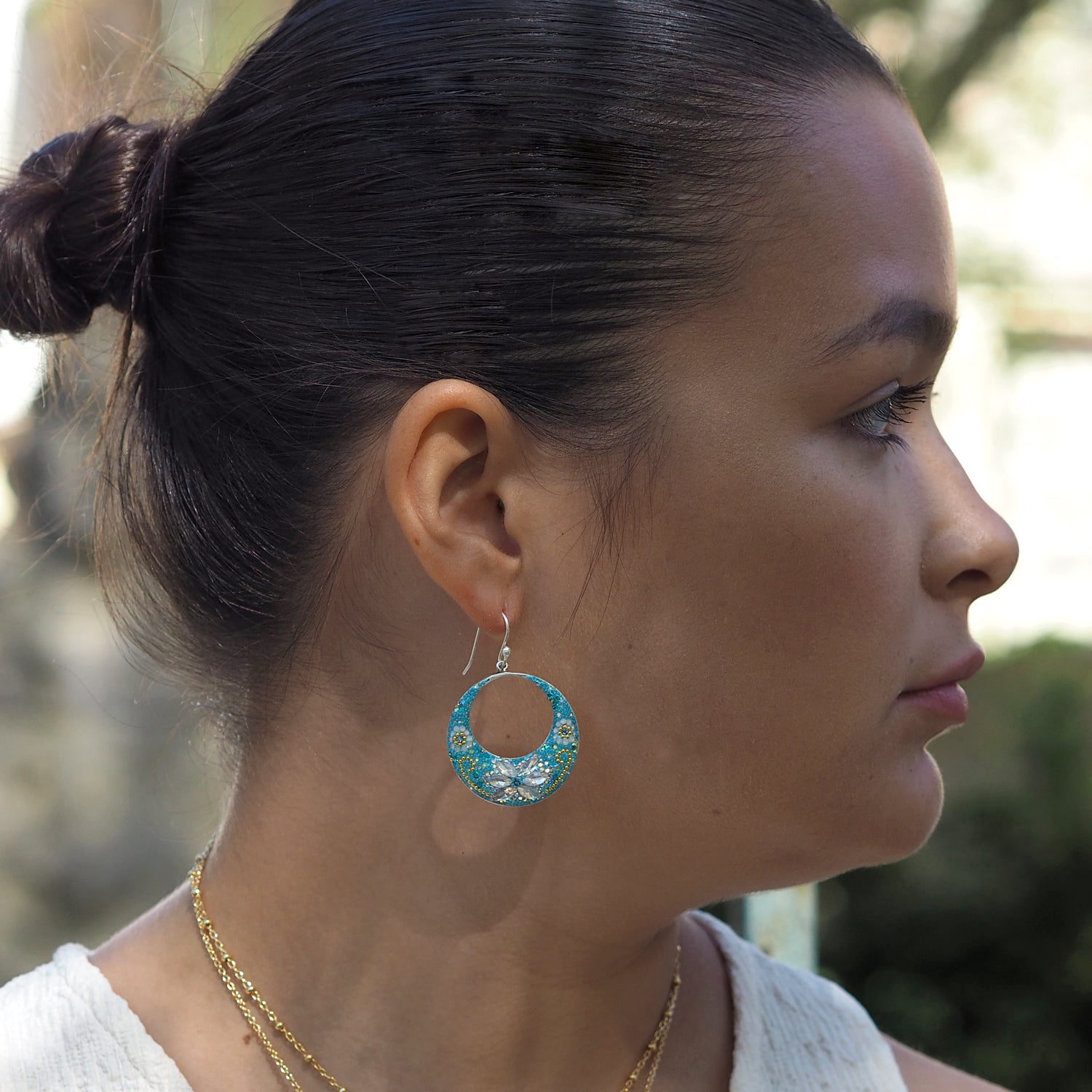 Close-up of a woman wearing turquoise hoop earrings with a blurred natural background