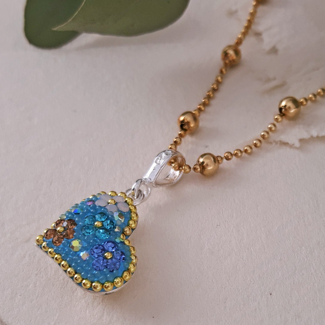 close up detail of a turquoise daisy heart pendant on gold dotty chain